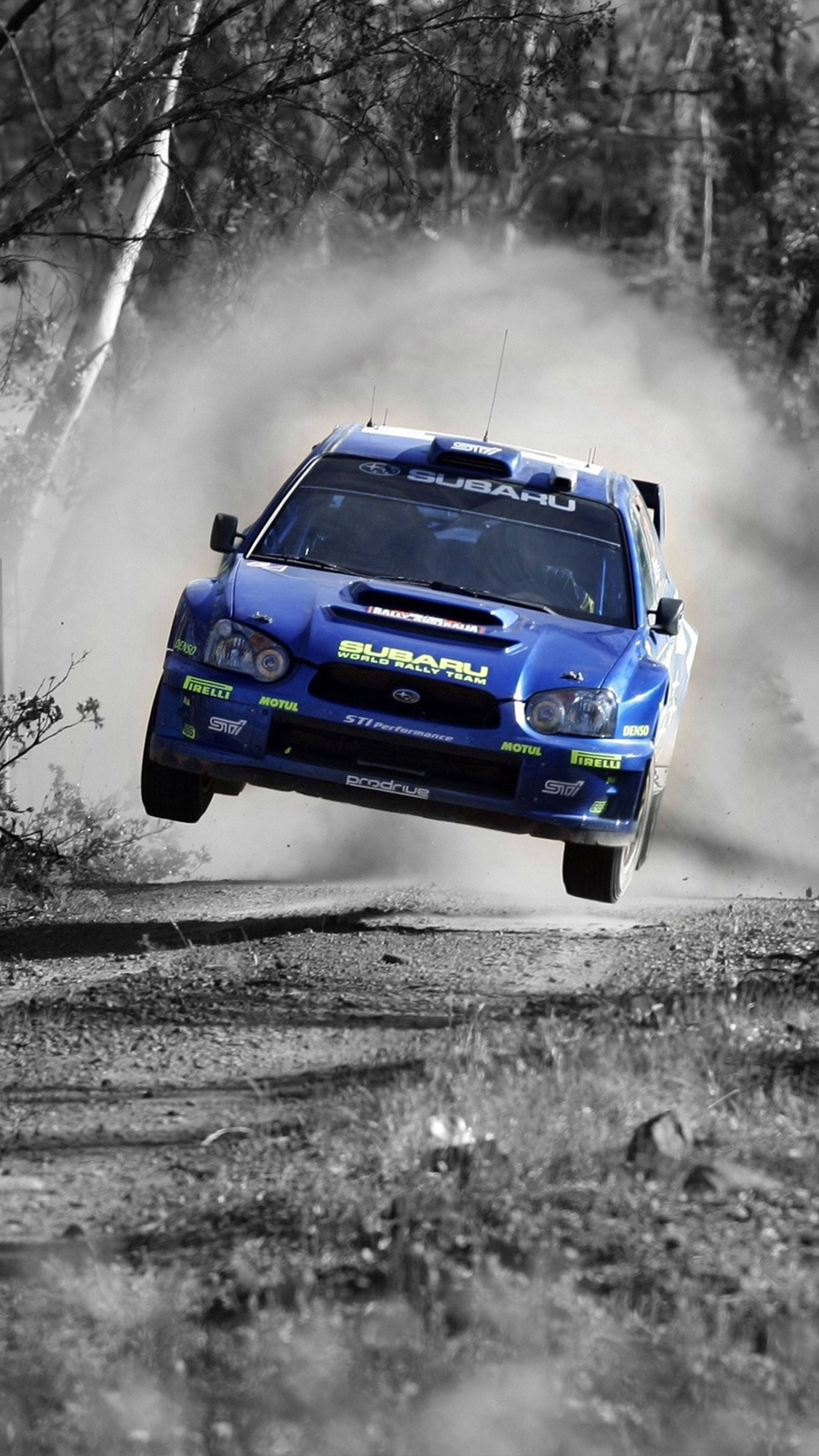 Auto Racing 桌布 壁紙 — 一輛藍色Subaru拉力賽車在塵土飛揚的林間小徑上飛躍，周圍樹木和薄霧繚繞。
