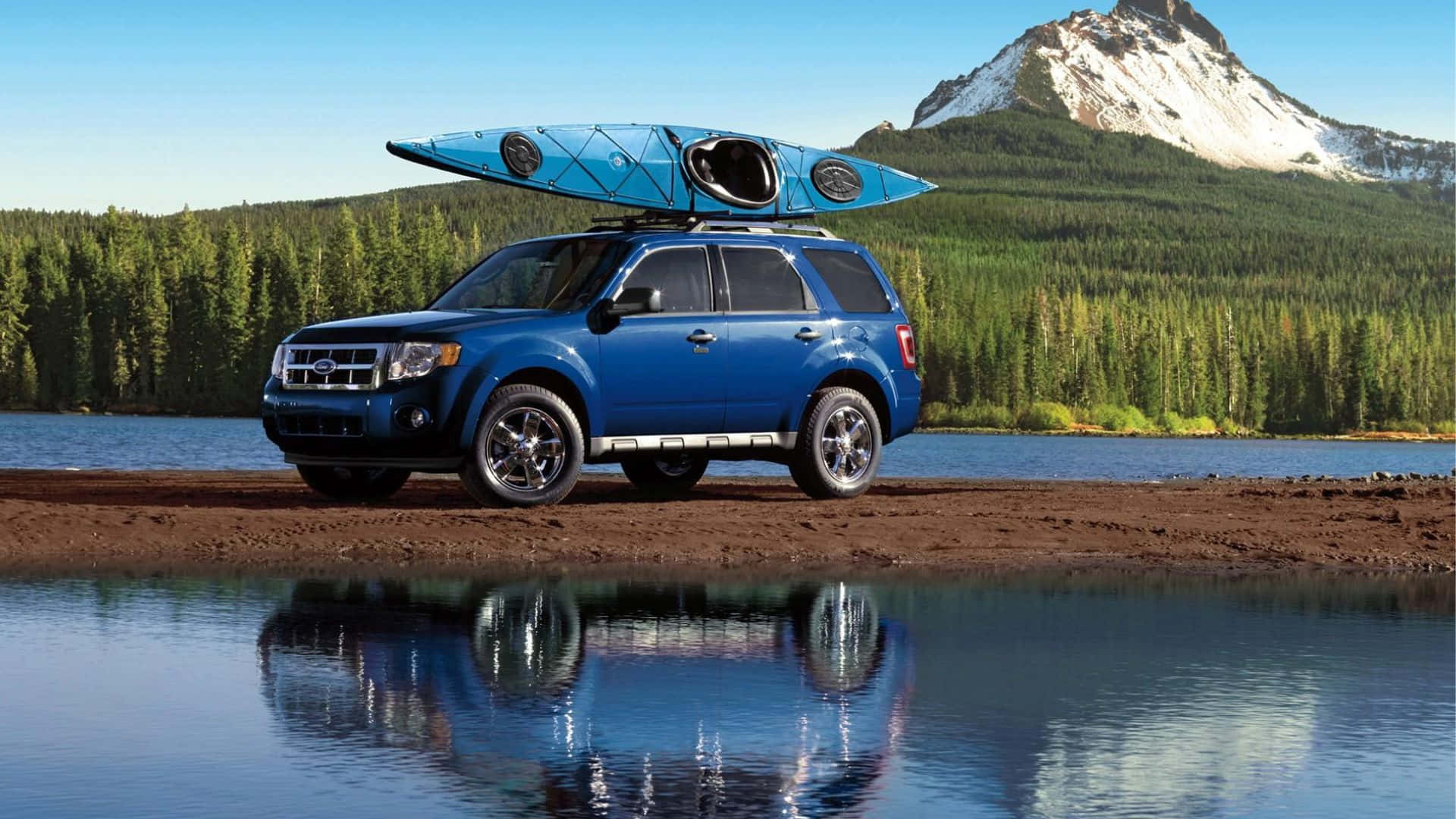 Ford Escape 桌布 壁紙 — 一輛藍色SUV車頂載著獨木舟，停在平靜的湖邊，湖面倒映著雪山和森林。