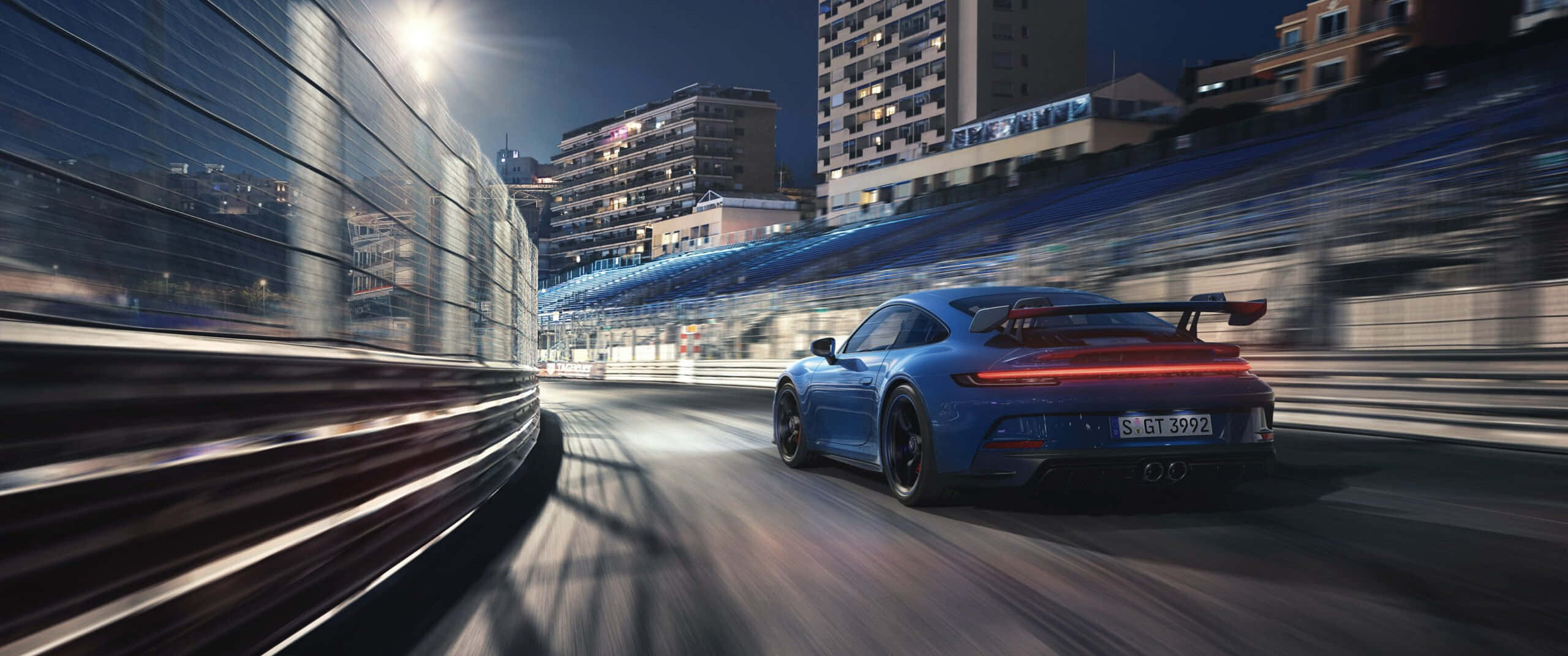 保時捷 桌布 壁紙 — 一輛藍色保時捷911 GT3 RS在夜間的城市賽道上奔馳，帶有動態模糊和發光的燈光。