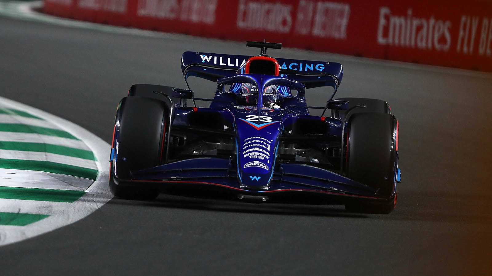 Racing 桌布 壁紙 — 一輛藍色和紅色的 Formula 1 賽車，號碼 23，在夜間於設有綠色和白色路緣的賽道上奔馳。