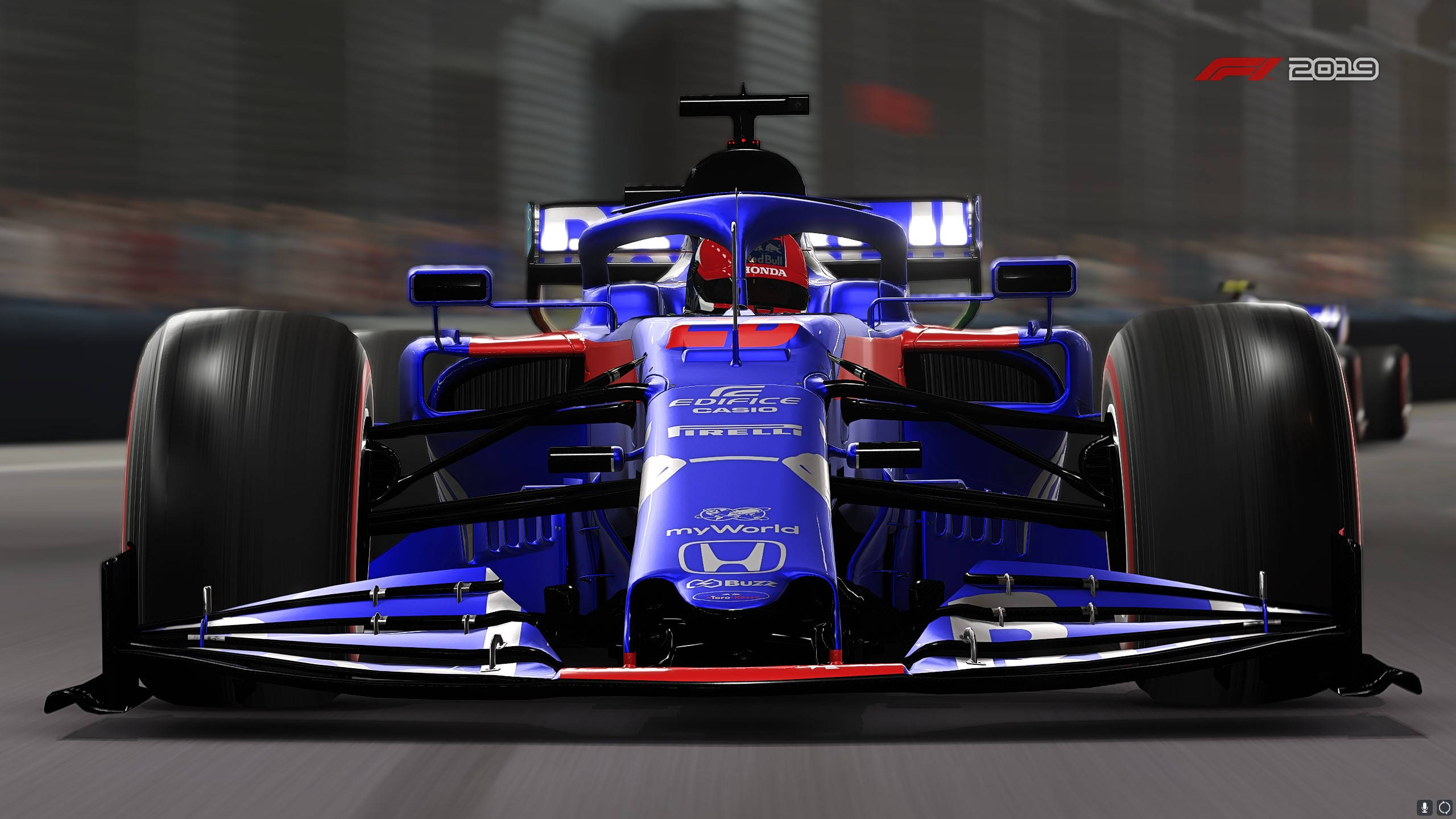 F1 2019 壁紙 桌布 壁紙 — 一輛藍色和紅色的一級方程式賽車在賽道上疾馳，背景是模糊的城市景觀。