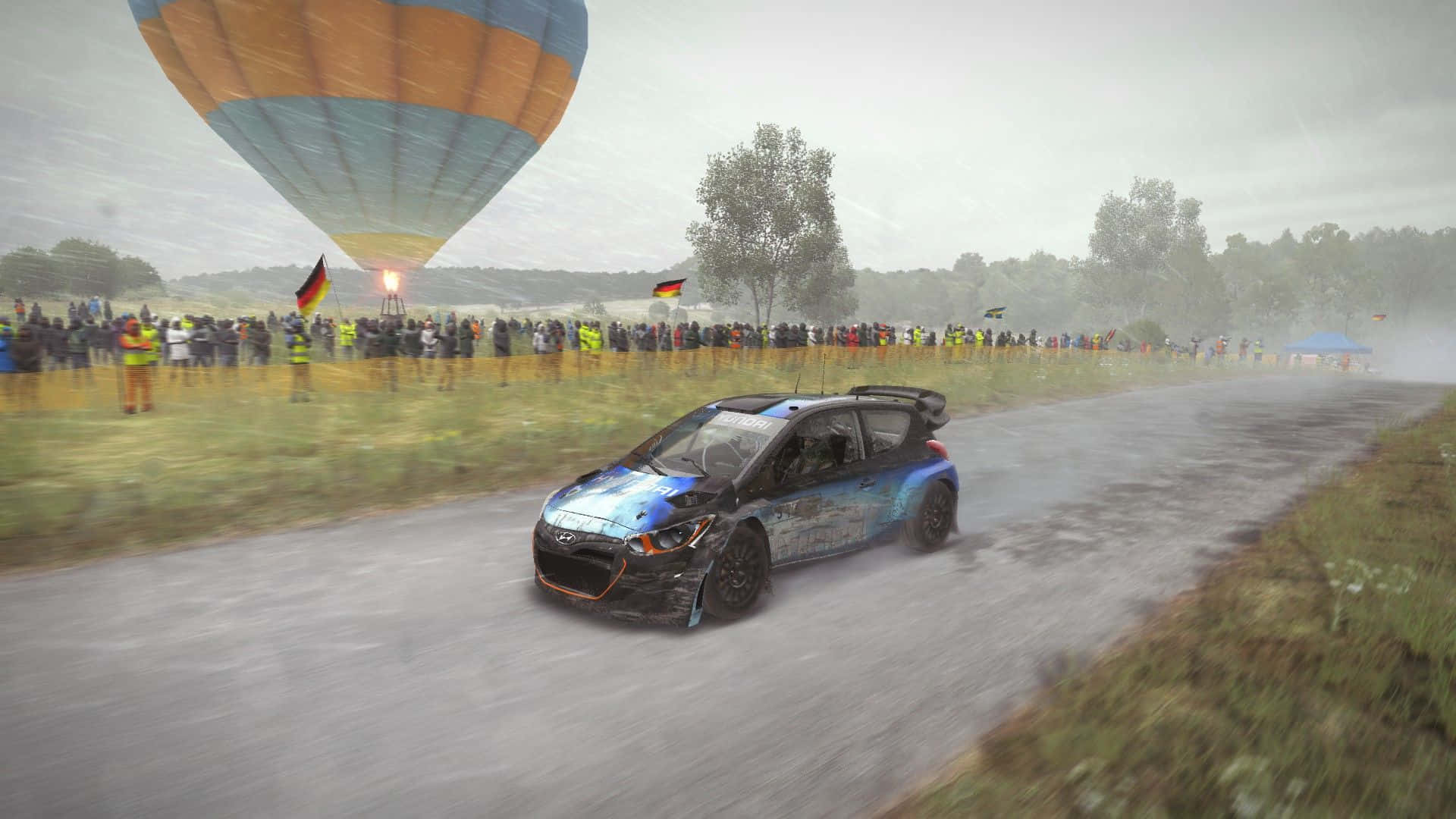 1920x1080 Dirt Rally 桌布 壁紙 — 一輛藍色拉力賽車在雨濕的鄉間飛馳，上空有熱氣球飄過，濕滑的道路兩旁站滿觀眾。
