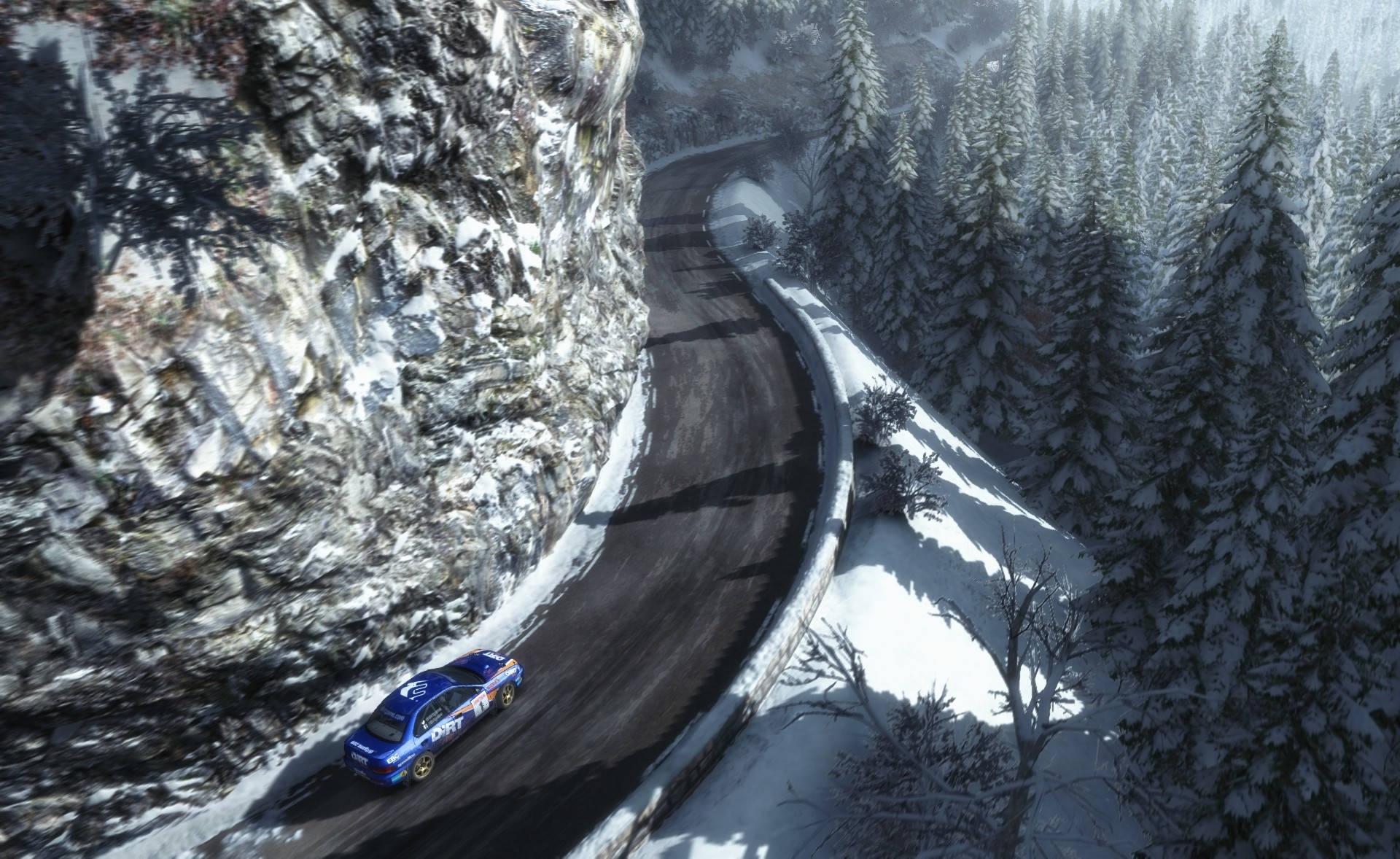 rally 桌布 壁紙 — 一輛藍色拉力賽車沿著蜿蜒的雪山道路飛馳，兩旁是白雪覆蓋的松樹和陡峭的岩石懸崖。