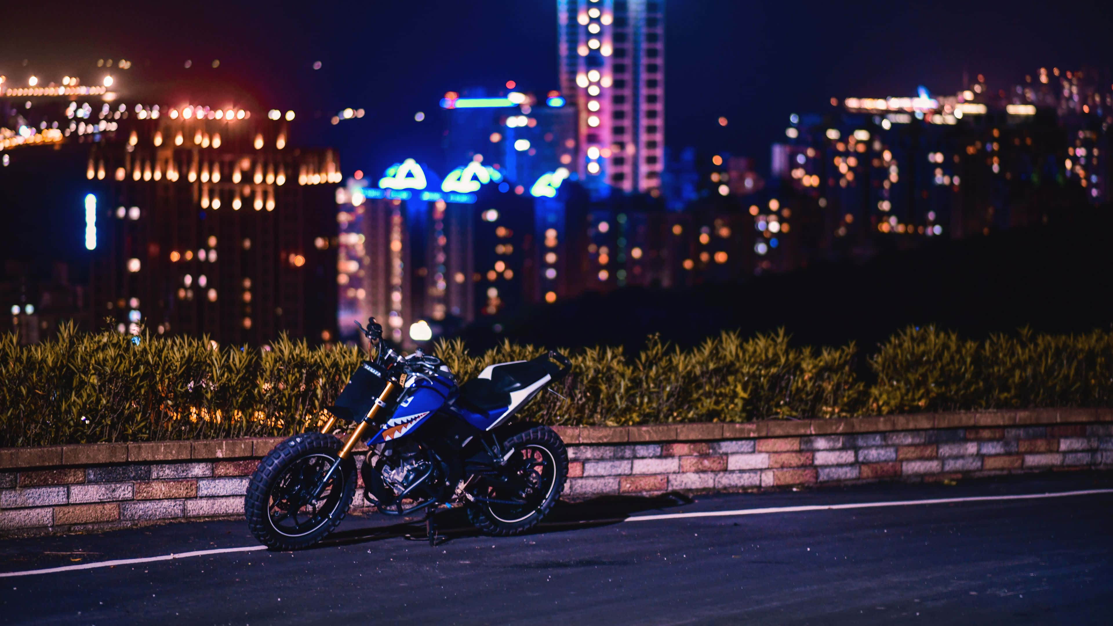 4K Bikes 桌布 壁紙 — 一輛藍色摩托車在夜間停泊在路邊，背後有充滿活力的散景城市景觀閃爍。
