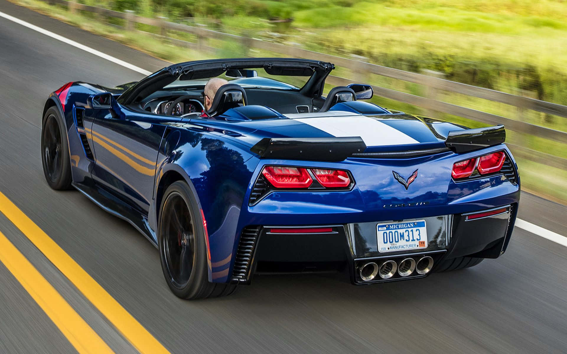 Chevrolet Corvette Grand Sport 桌布 壁紙 — 一輛藍色敞篷跑車在陽光明媚的高速公路上疾馳，模糊的綠樹從旁掠過。