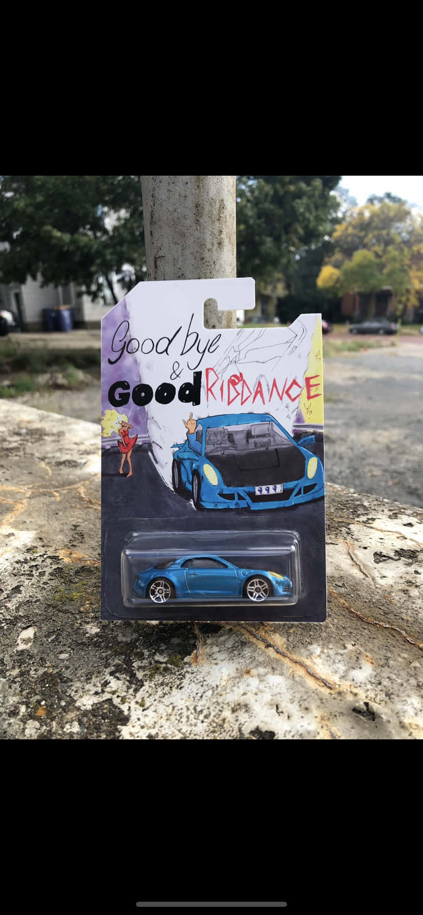 Goodbye And Good Riddance 桌布 壁紙 — 一輛藍色玩具跑車連包裝，上面印有「Goodbye & Good Riddance」字樣，放在戶外風化的混凝土表面上。