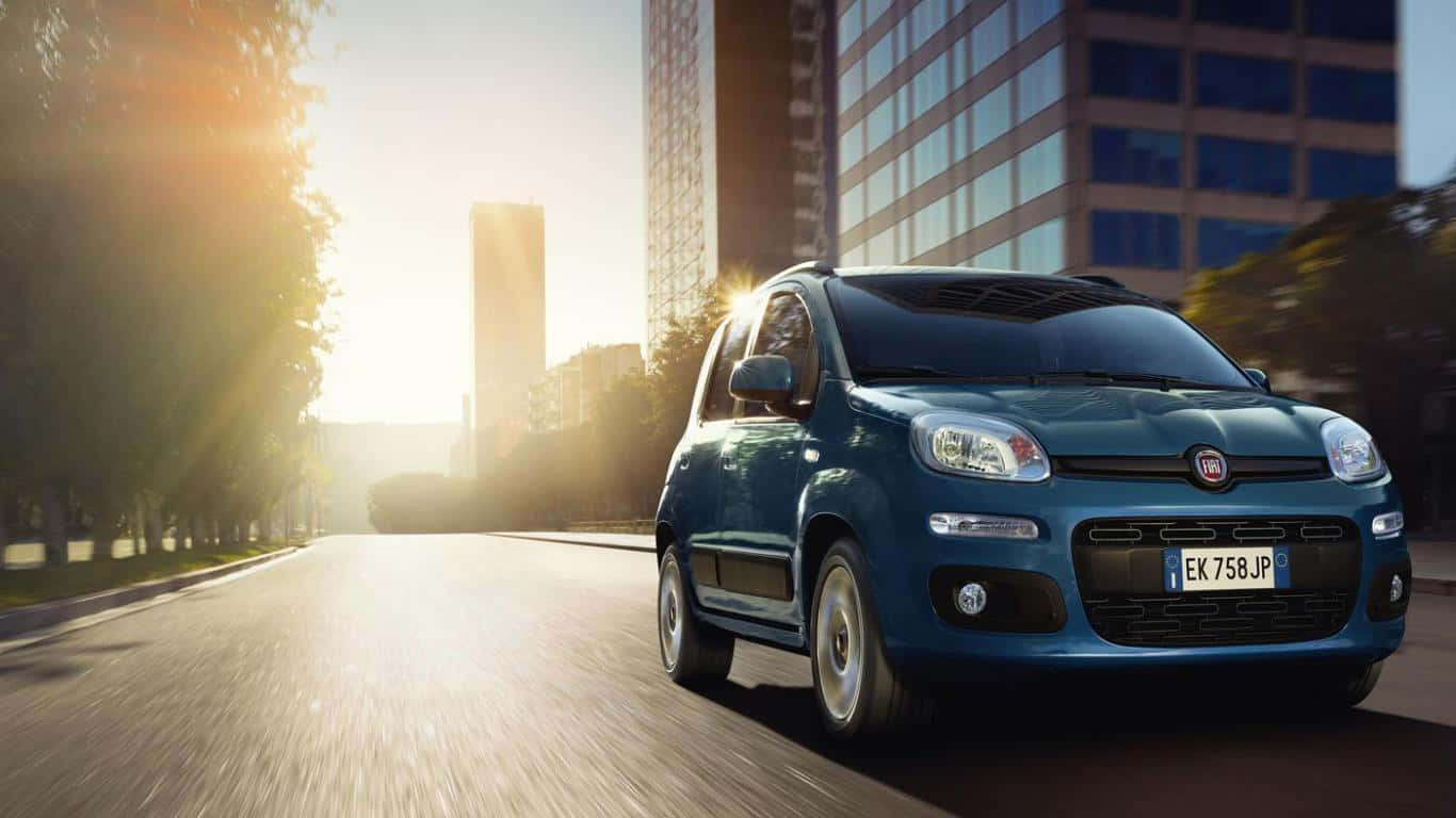 Fiat Panda 桌布 壁紙 — 一輛藍色的Fiat Panda在陽光明媚的城市街道上行駛，兩旁有現代建築和樹木。