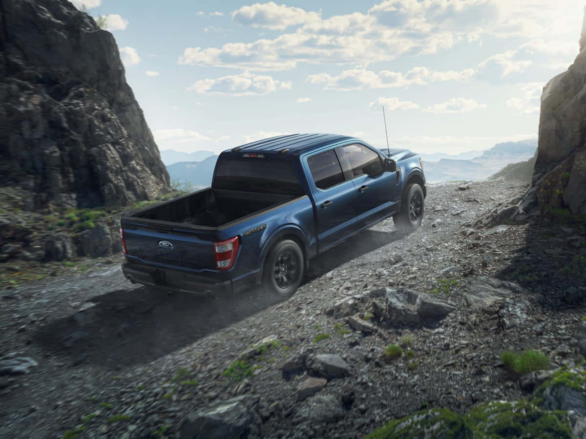 Cliff 桌布 壁紙 — 一輛藍色福特 F-150 Raptor 卡車在明亮多雲的天空下，強勁地駛過岩石山隘。