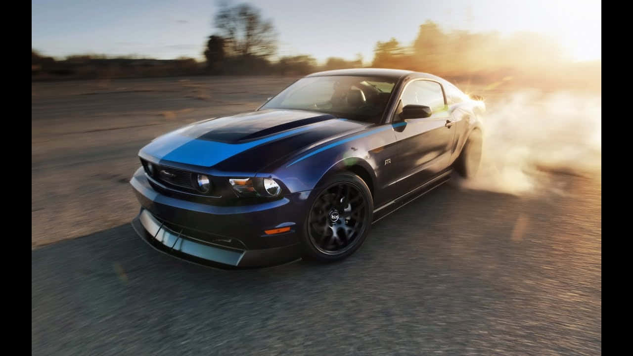 Compact Car 桌布 壁紙 — 一輛藍色福特Mustang GT在塵土飛揚的道路上甩尾，後輪冒出滾滾濃煙，正值黃金時刻。