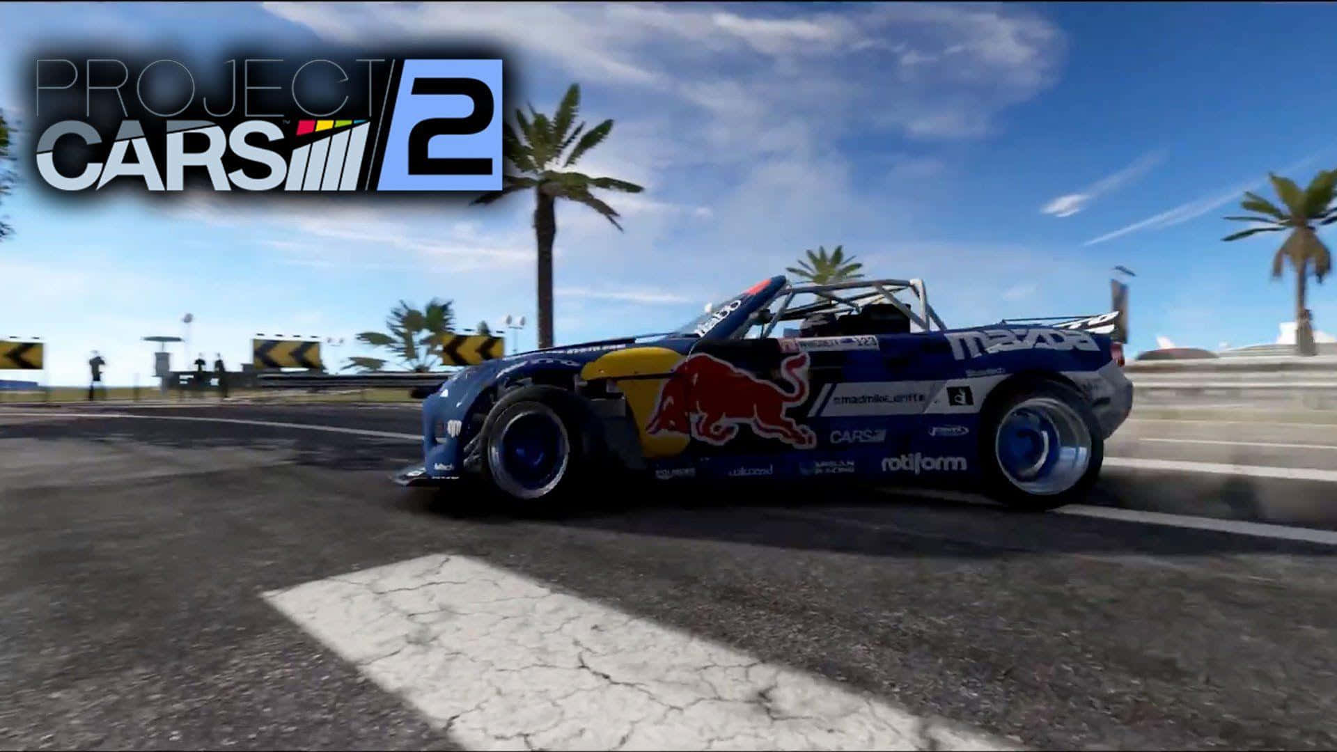 Best Project Cars 2 桌布 壁紙 — 一輛藍色紅牛賽車在陽光明媚的海岸賽道上飄移，棕櫚樹和遊戲標誌清晰可見。