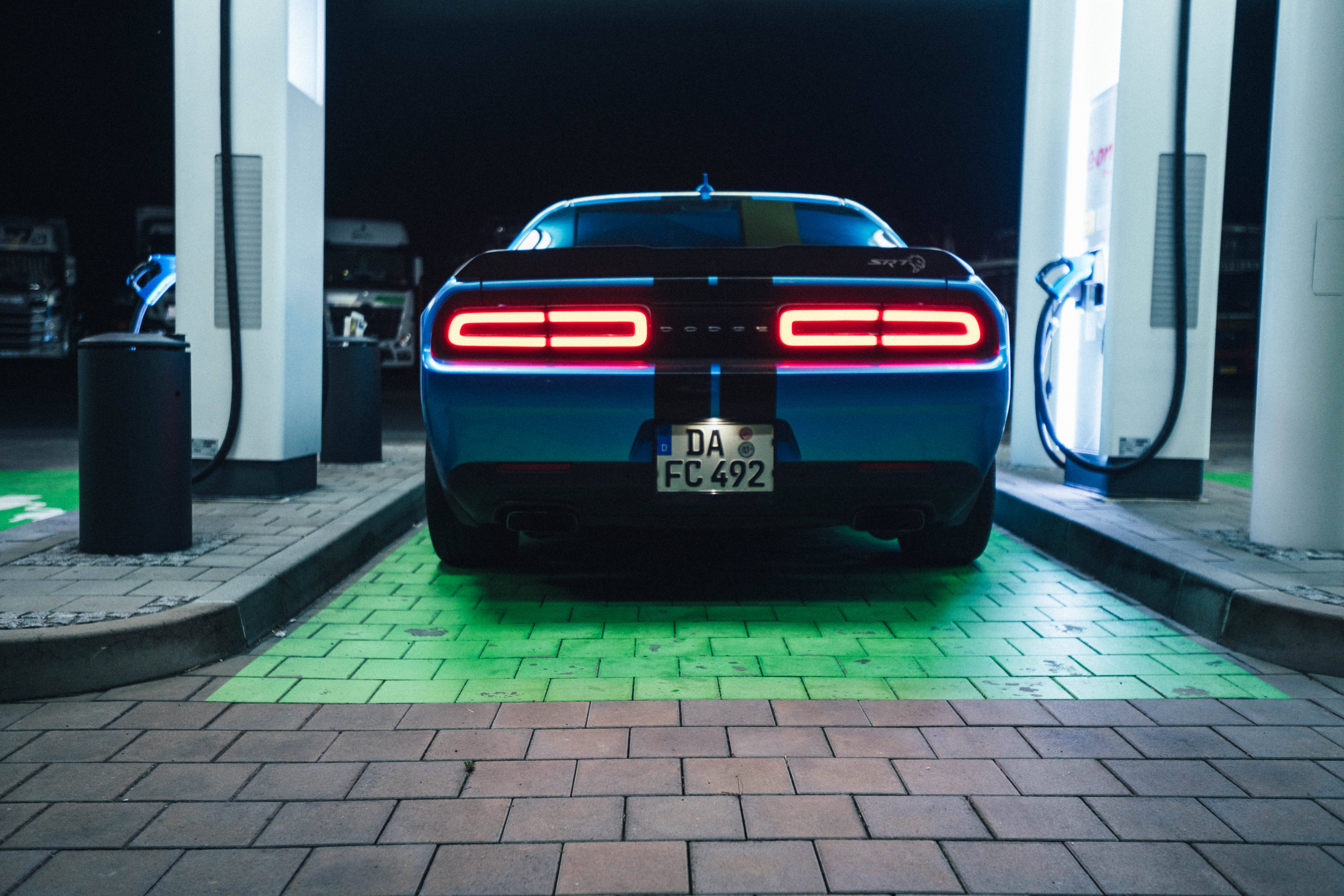 Challenger 桌布 壁紙 — 一輛藍色肌肉車在夜間燈光下停放在現代電動充電站，紅色尾燈發光。