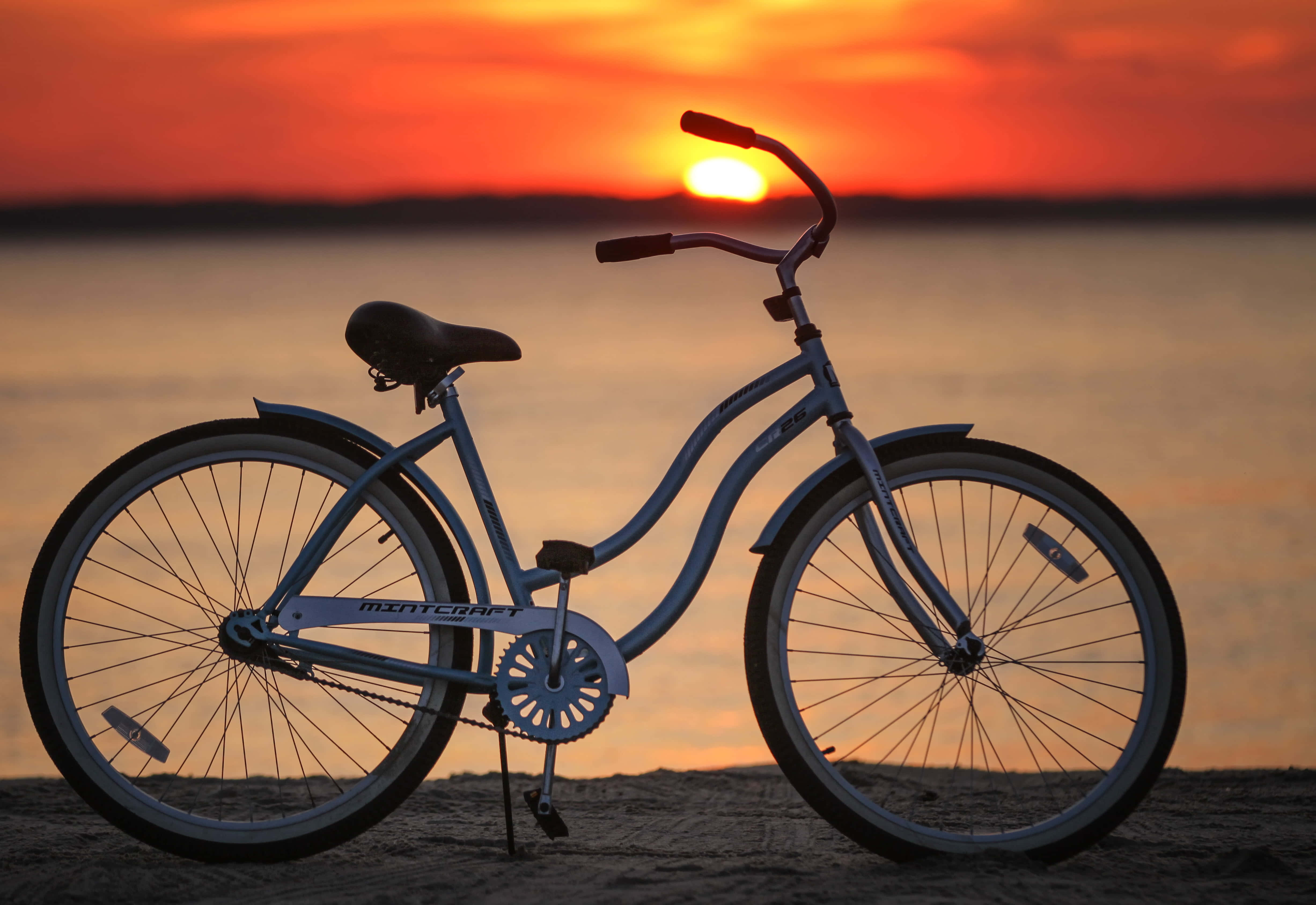 Beach Cruiser 桌布 壁紙 — 一輛藍色腳踏車在海灘上呈現剪影，太陽以火熱的橙色和紅色色調在水面上落下。
