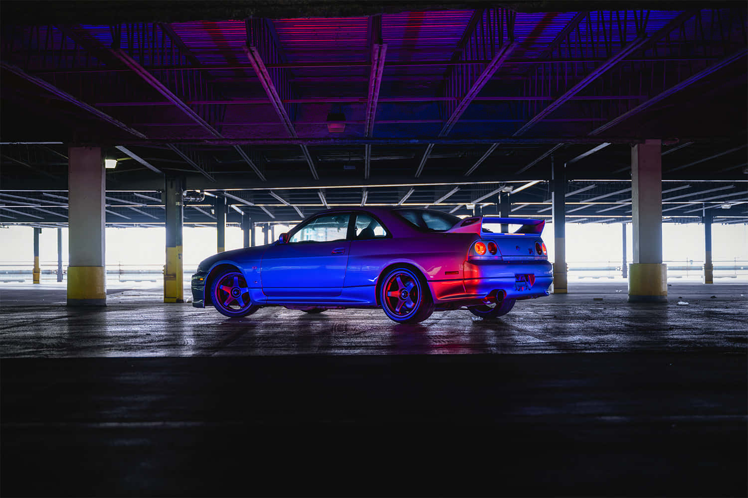 R33 GT-R 桌布 壁紙 — 一輛藍色跑車在昏暗的地下停車場中，在霓虹紫色和粉紅色燈光下閃耀。
