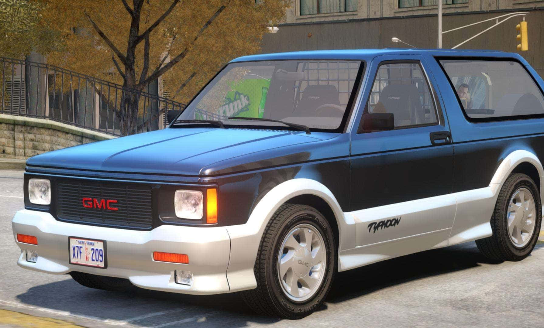 Gmc Typhoon 桌布 壁紙 — 一輛藍銀色GMC Typhoon旅行車停在城市街道上，背景有秋樹和交通號誌。