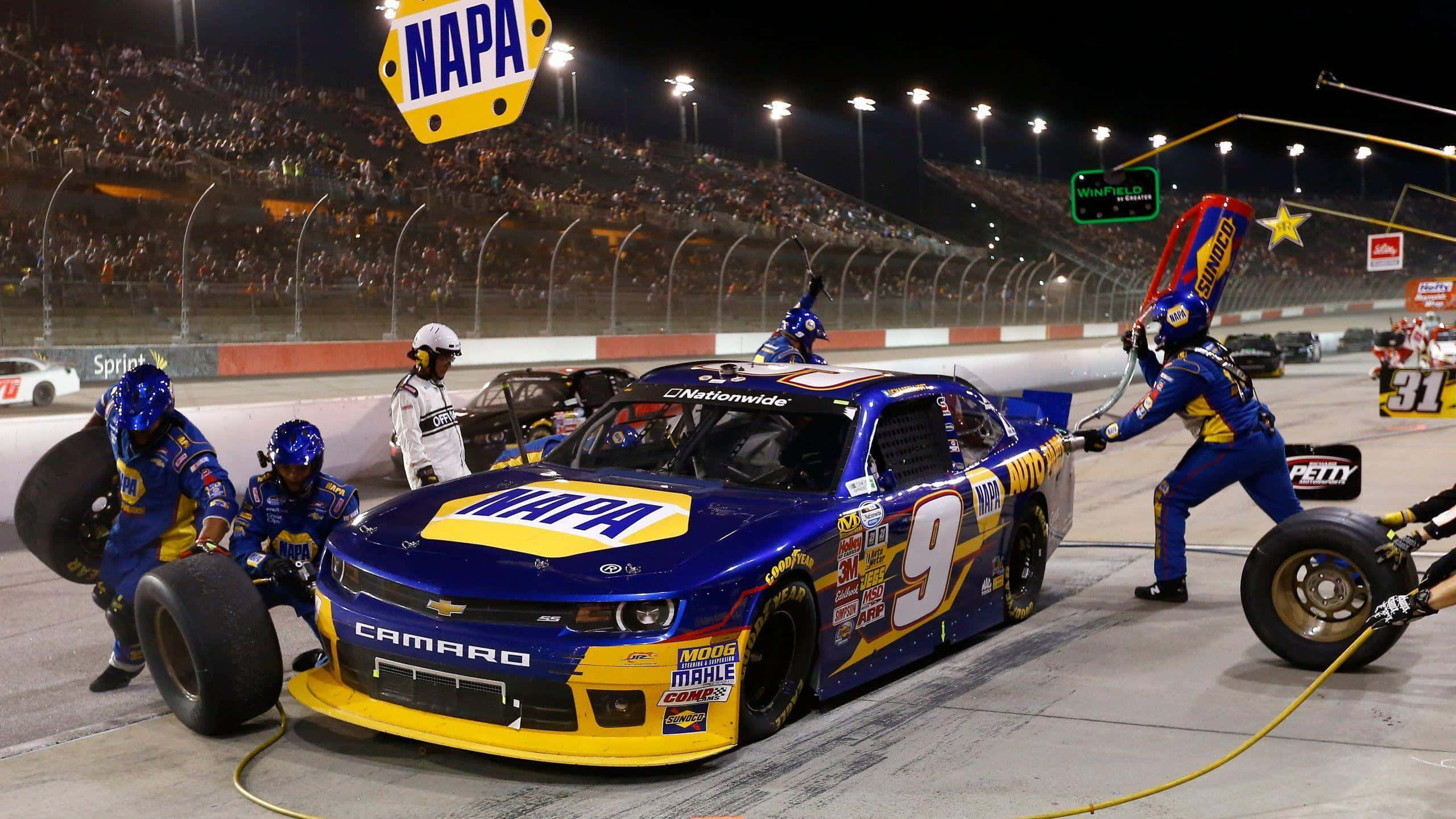 nascar 桌布 壁紙 — 一輛藍黃色、編號9的NASCAR賽車在夜間明亮的體育場燈光下由維修站工作人員進行維修。