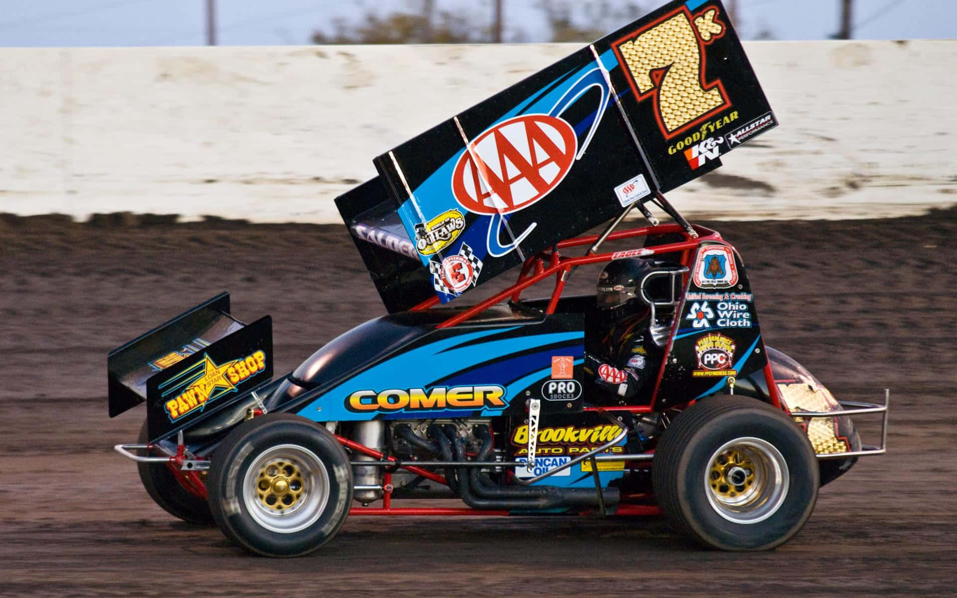Sprint Car Racing 桌布 壁紙 — 一輛藍黑相間、編號7的衝刺賽車在明亮的日光下於泥地賽道上比賽。