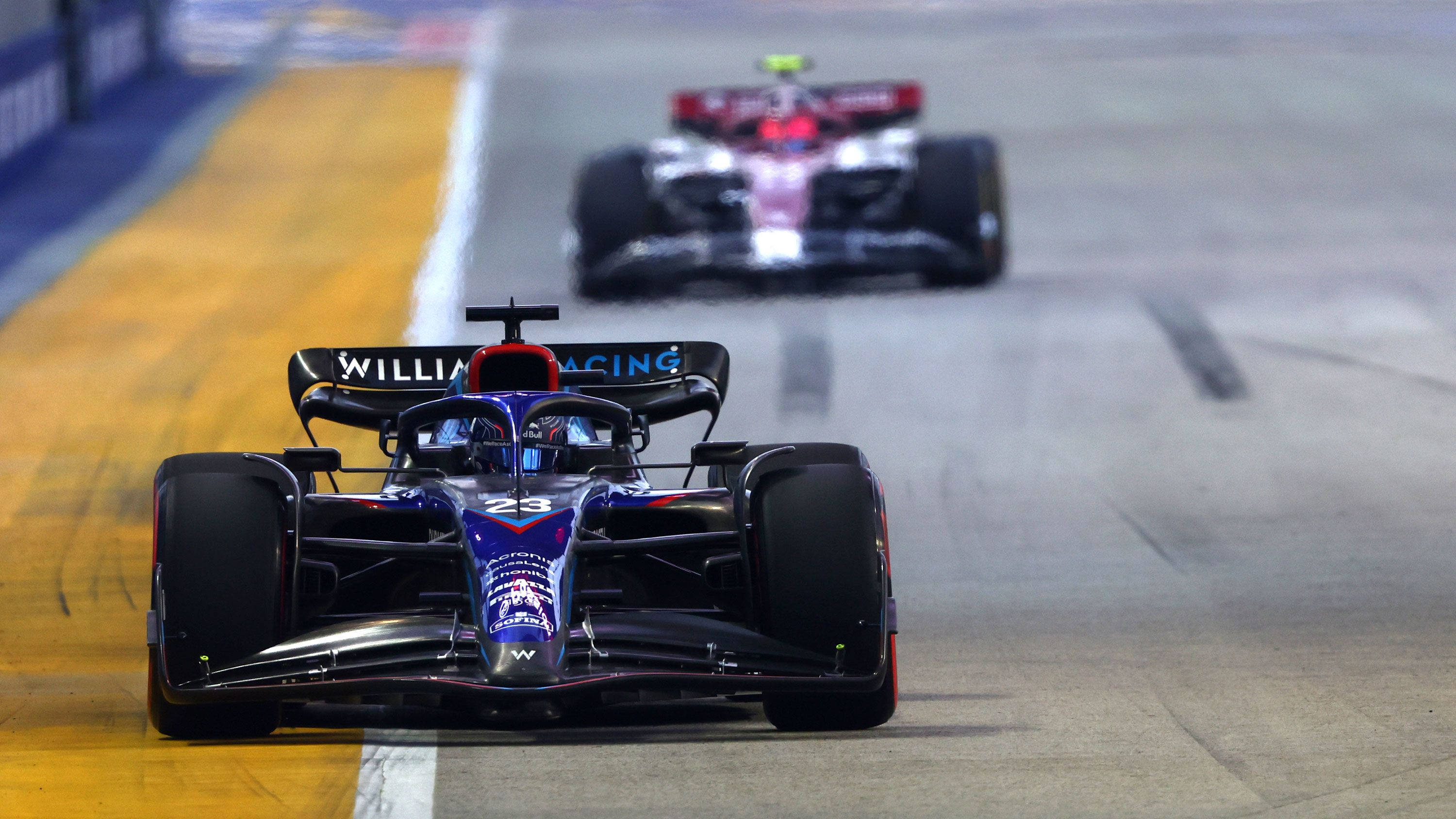 F1 桌布 壁紙 — 一輛藍黑相間的F1賽車（編號23）在夜間賽道上緊跟在紅白相間的對手後面比賽。