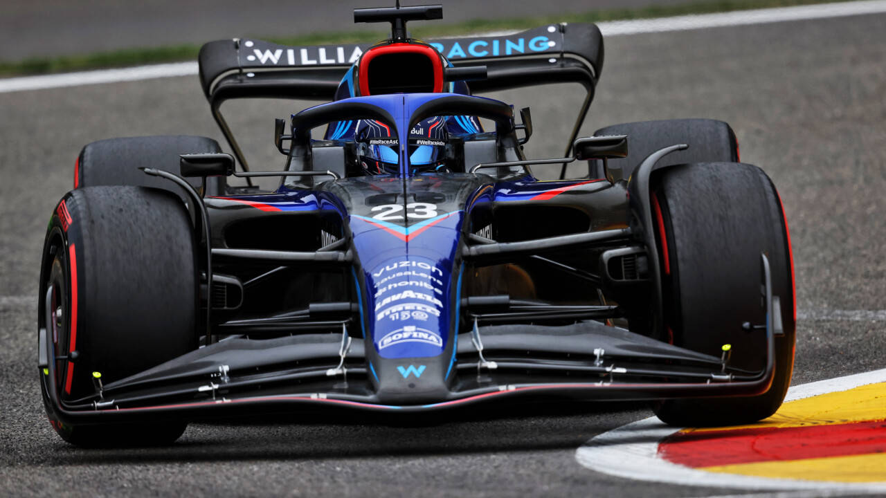 Racing 桌布 壁紙 — 一輛藍黑相間的F1賽車（編號23）在潮濕的賽道上行駛，靠近紅、黃、白色的路緣石。
