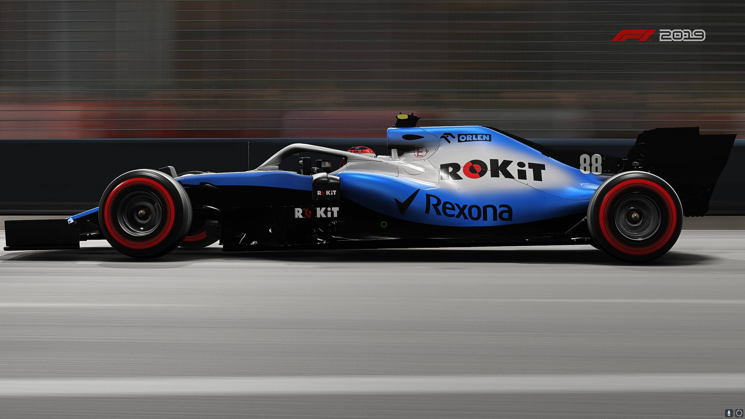 F1 2019 壁紙 桌布 壁紙 — 一輛藍黑配色的F1賽車，紅色輪胎，在賽道上疾馳，背景呈現動態模糊效果。
