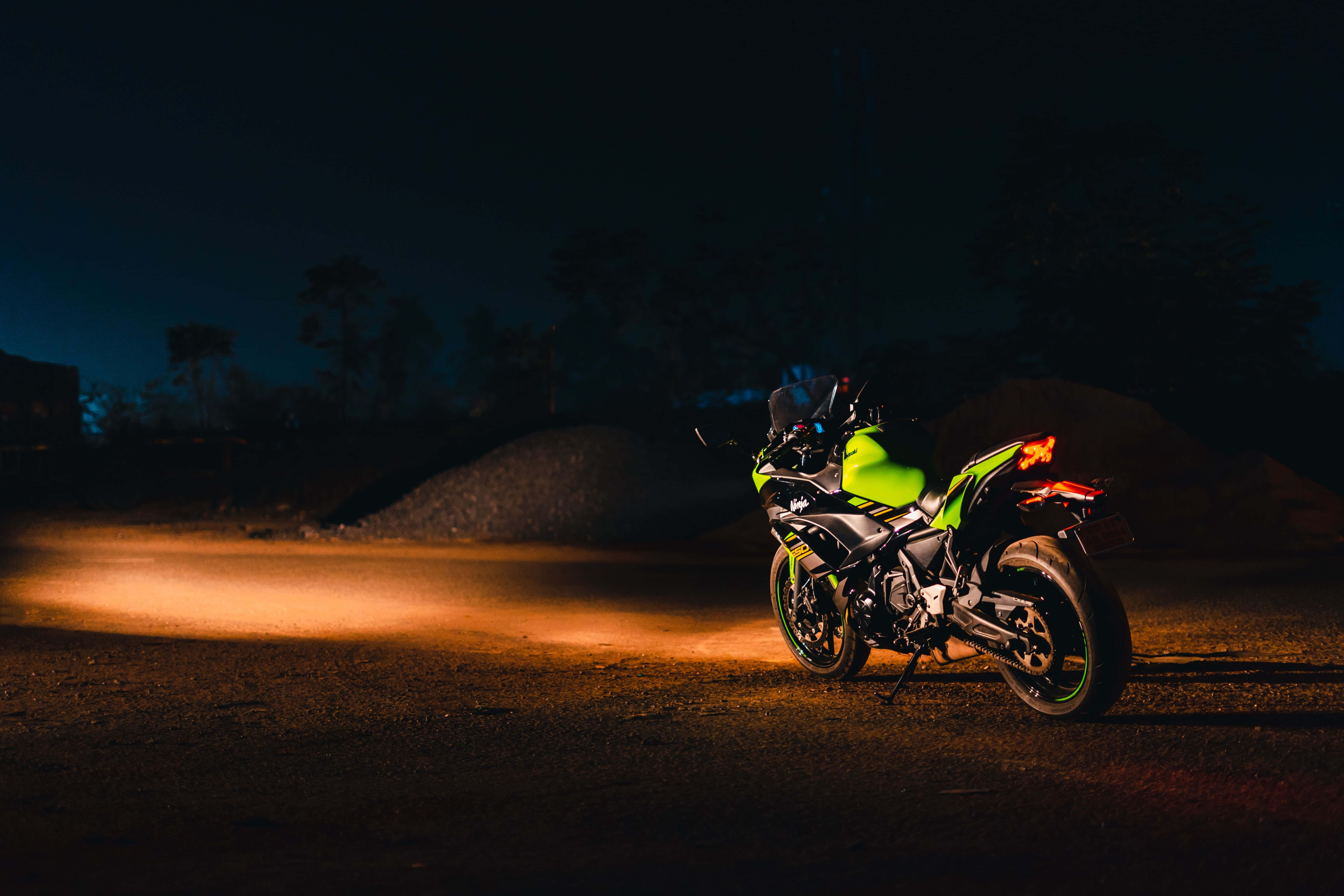 motorbike 桌布 壁紙 — 一輛螢光綠色的機車在夜間黑暗的碎石路上，在其車頭燈下發光，背景有樹木。