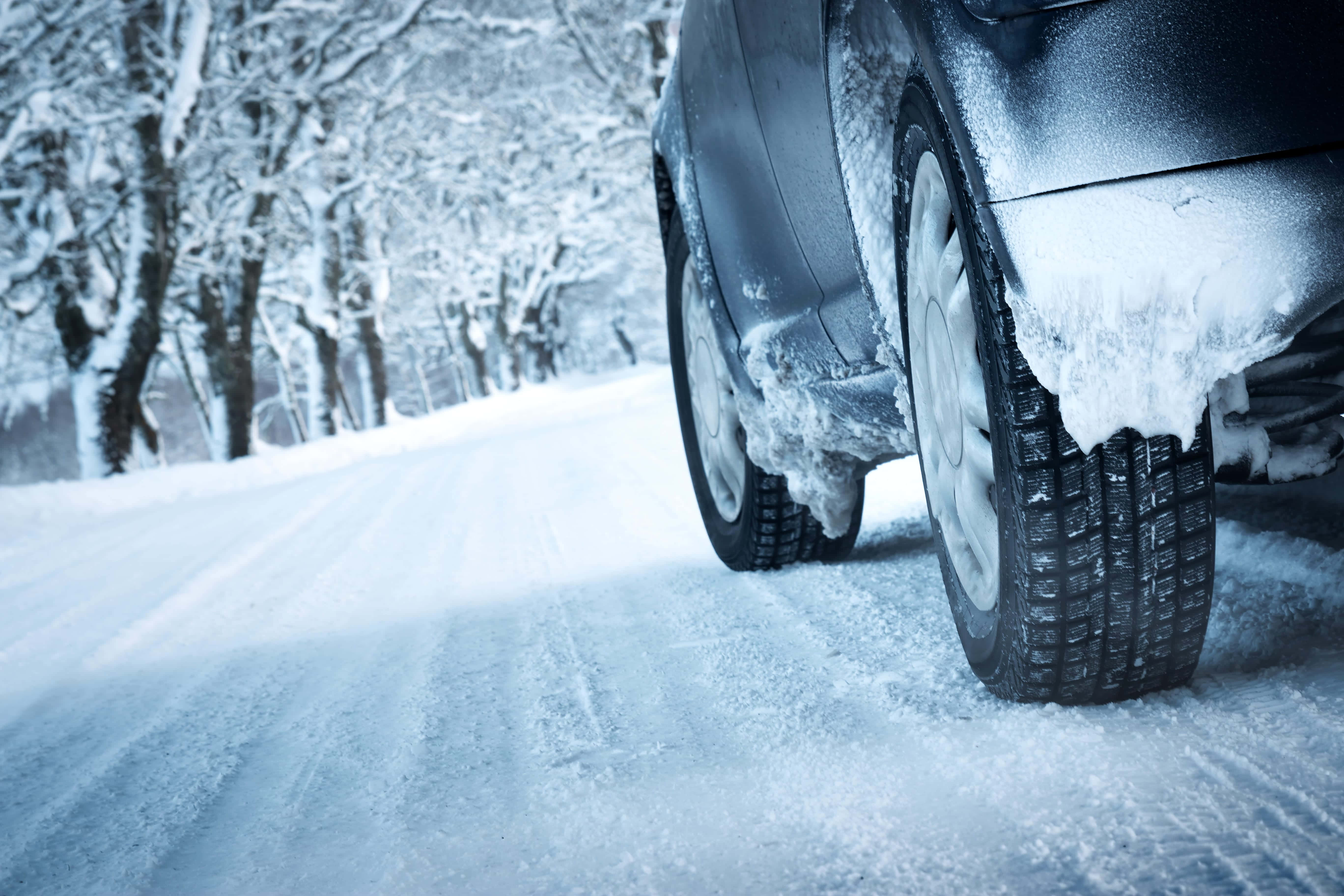 Winter Driving 桌布 壁紙 — 一輛被雪覆蓋的汽車的後輪在寒冷的冬日天空下，抓緊一條兩旁滿是積雪樹木的冰凍道路。