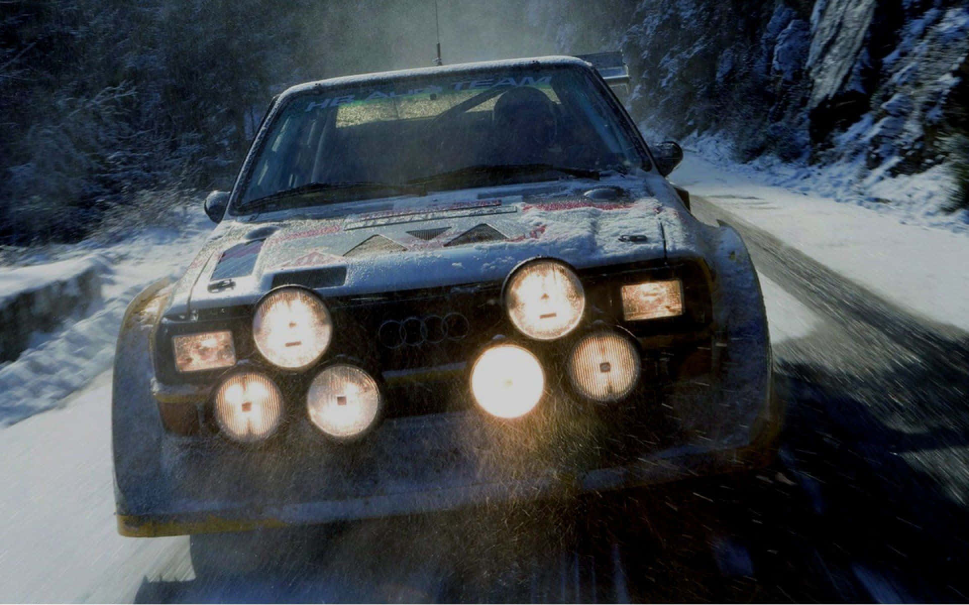 Ice Racing 桌布 壁紙 — 一輛覆蓋著積雪的拉力賽車，亮著明亮的車頭燈，在兩旁積雪樹木環繞的蜿蜒山路上飛馳。