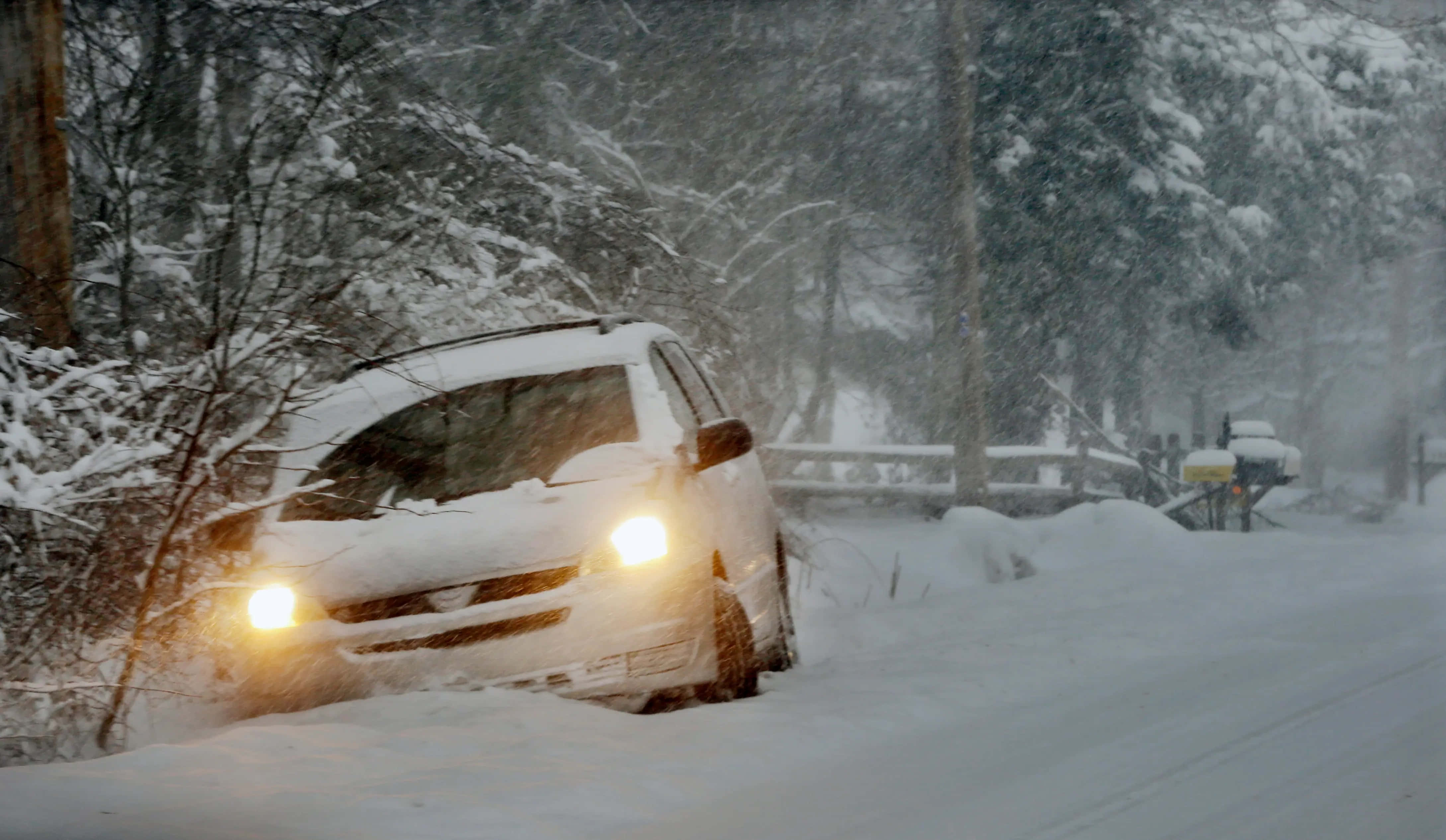 Winter Driving 桌布 壁紙 — 一輛覆蓋著雪的汽車，車頭燈閃爍，在森林道路上的暴風雪中掙扎前行。