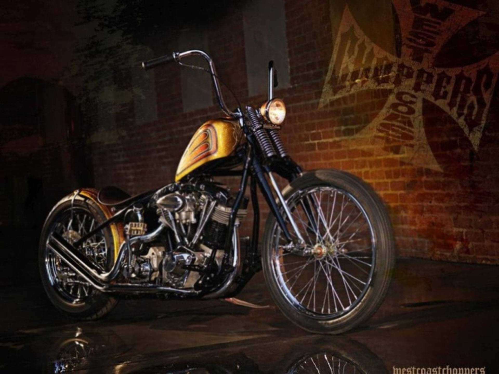 Choppers 桌布 壁紙 — 一輛訂製的chopper摩托車，金色火焰塗裝在聚光燈下閃閃發光，背景是帶有褪色塗鴉的磚牆。