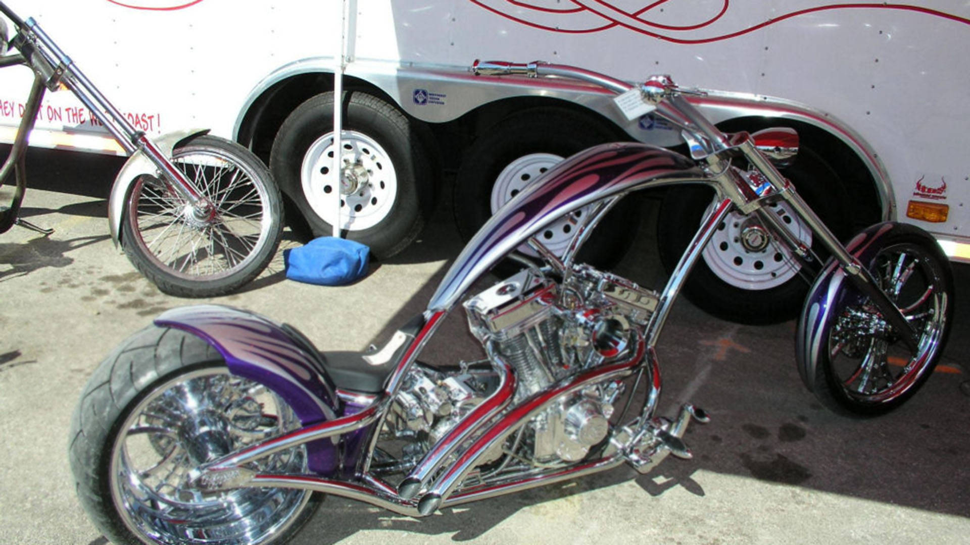 Choppers 桌布 壁紙 — 一輛訂製的chopper摩托車，帶有鉻和紫色火焰塗裝，在明亮的陽光下於白色拖車旁閃閃發光。