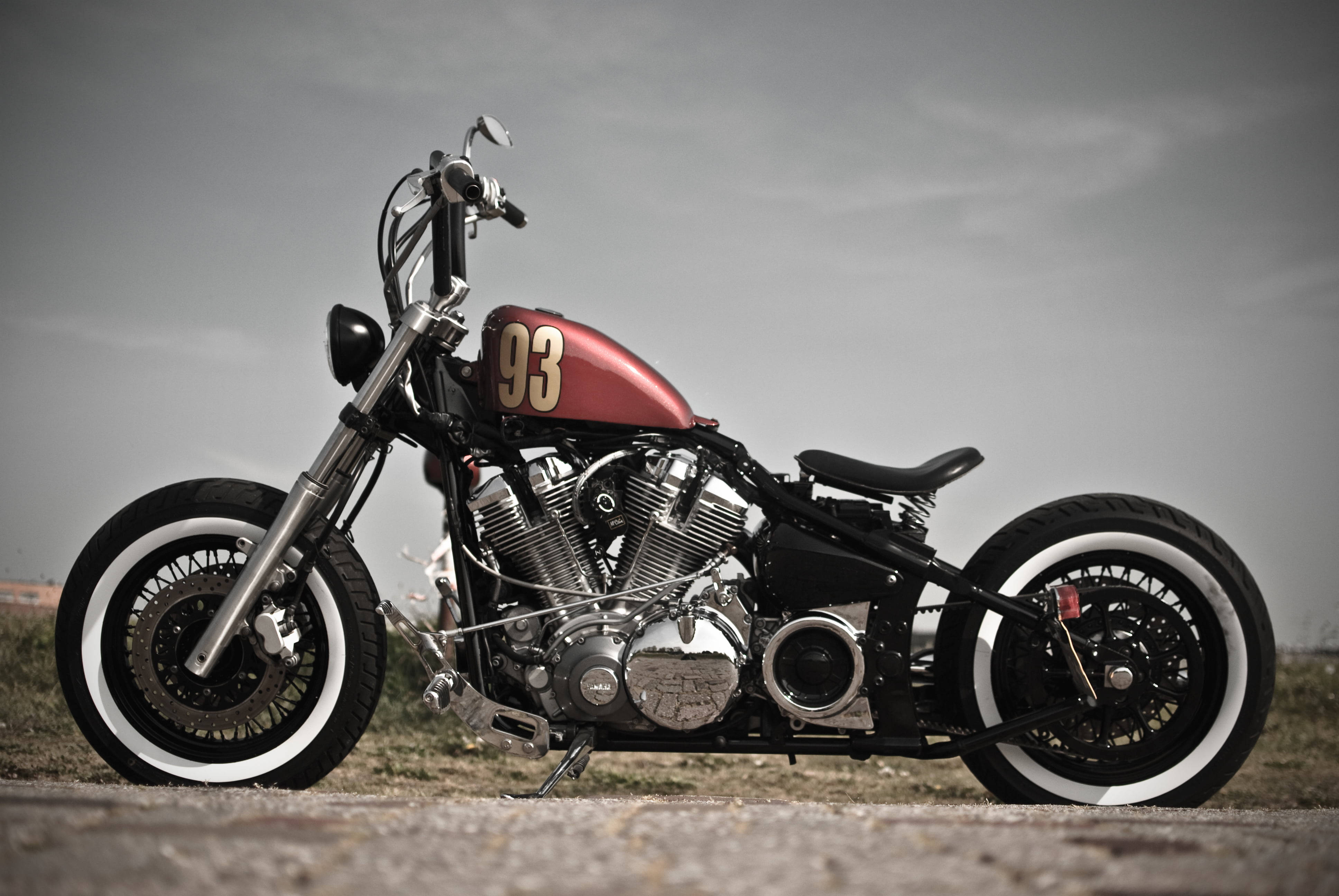 Bobber 桌布 壁紙 — 一輛訂製的chopper摩托車，紅色油箱標記93，停在碎石路上，天色陰沉。