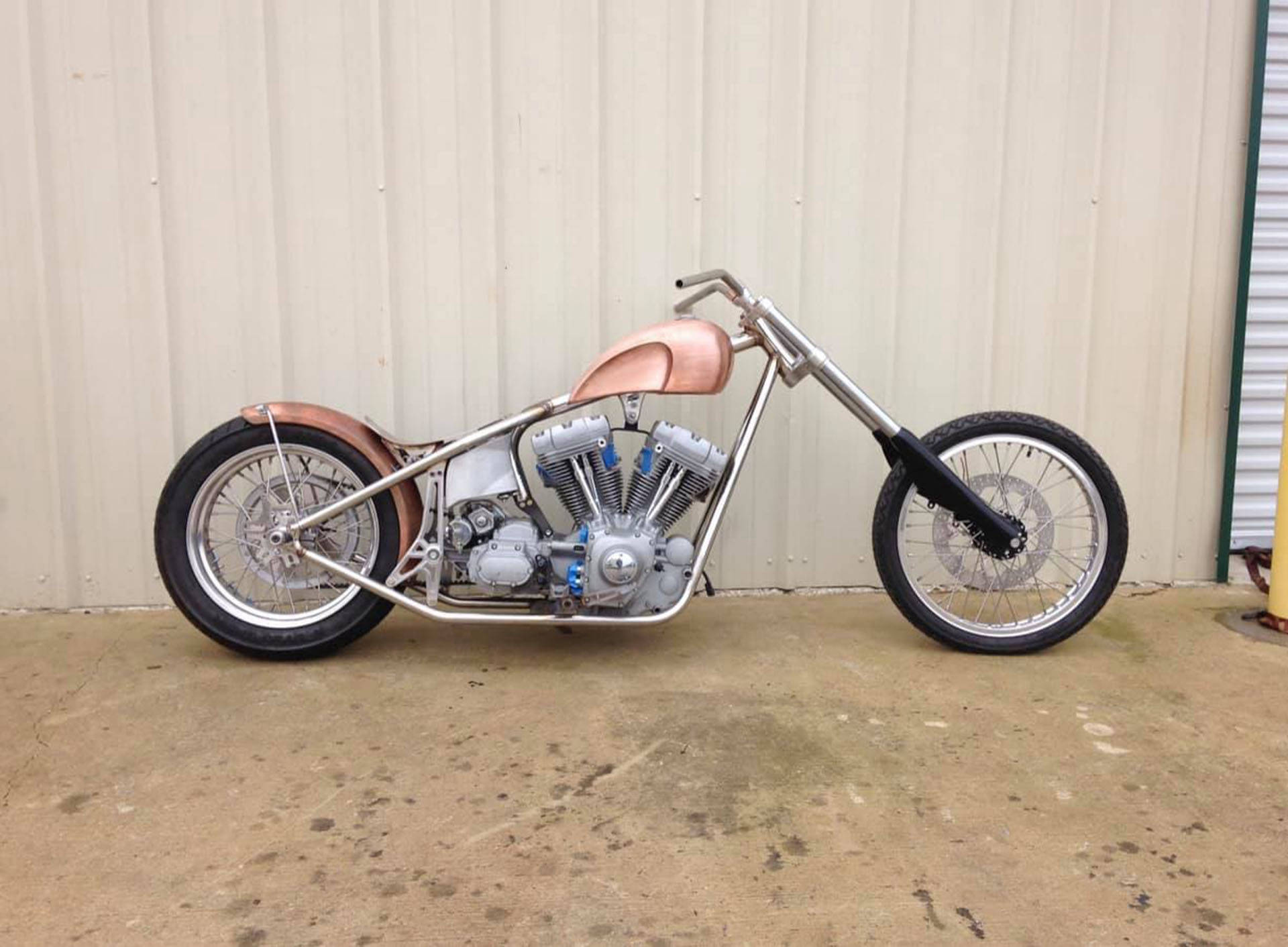 Choppers 桌布 壁紙 — 一輛訂製的chopper機車，帶有銅色點綴和鉻合金細節，停靠在米色金屬牆邊。