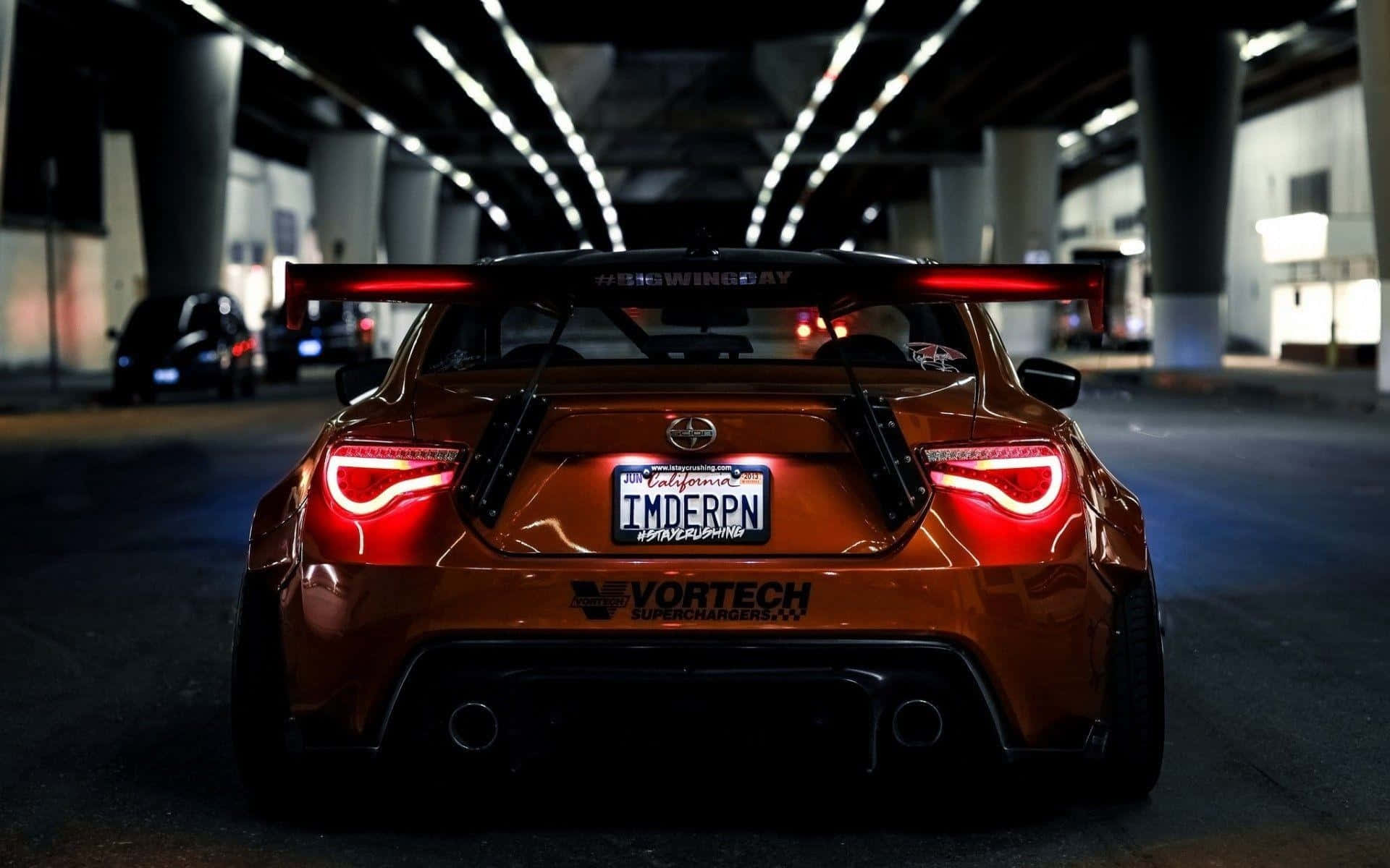 訂製的橙色跑車，帶有紅色尾燈，停放在黑暗的城市天橋下。 — Toyota Supra Mk4 壁紙