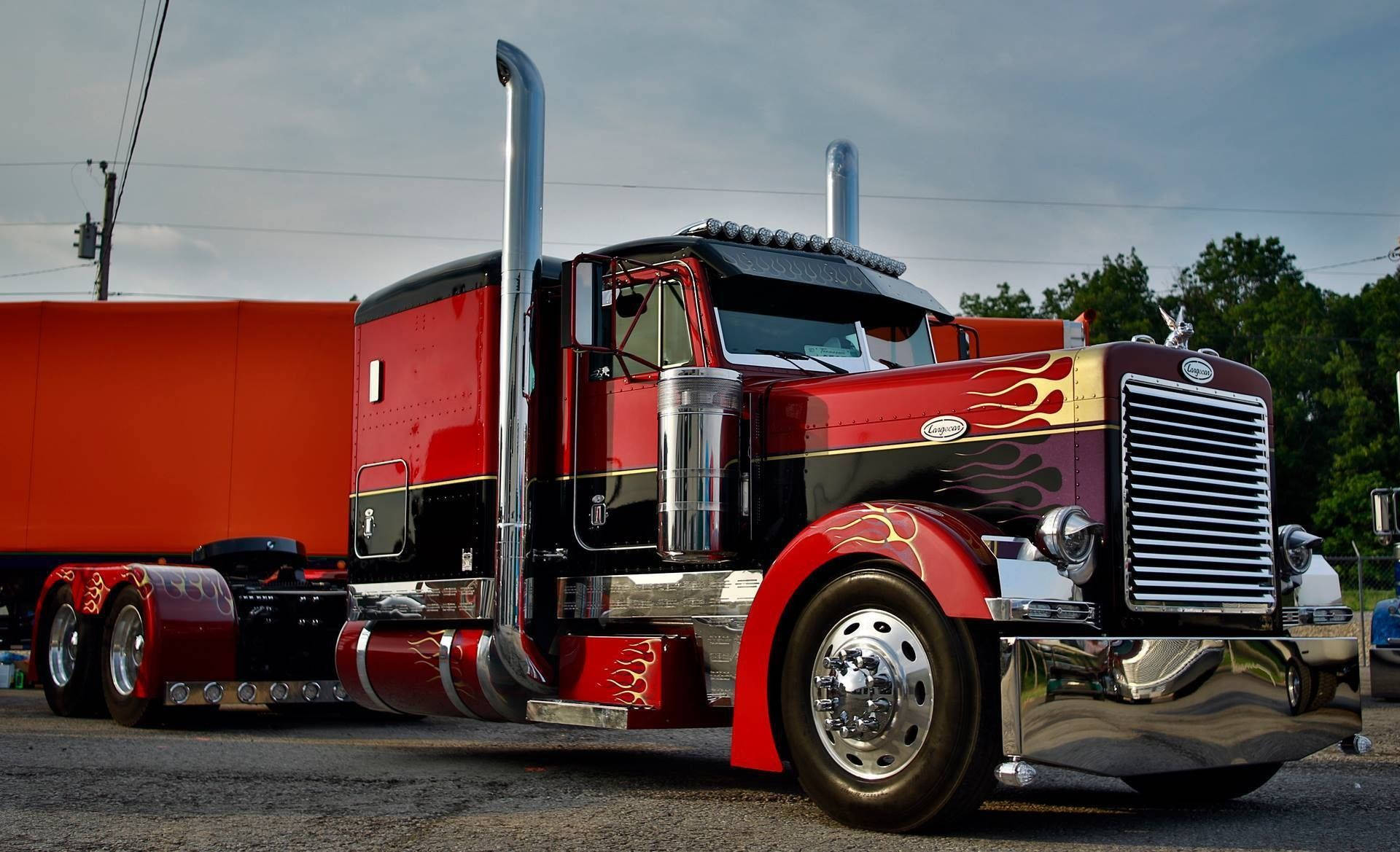 Peterbilt 桌布 壁紙 — 一輛訂製的紅色和黑色半掛卡車，帶有鍍鉻裝飾和火焰貼花，停在橙色拖車旁邊，天空多雲。