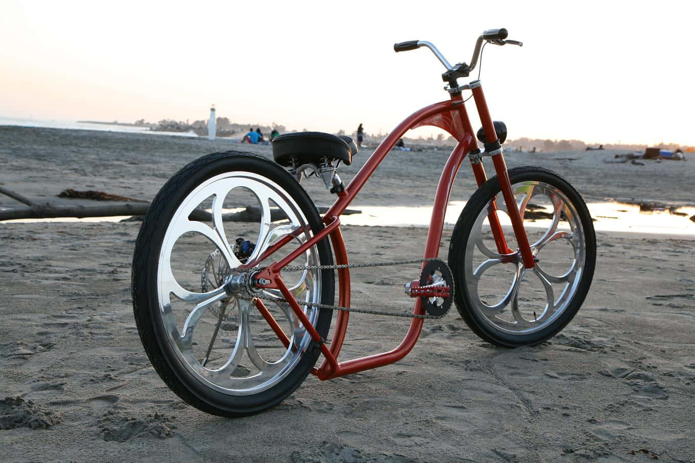 Beach Cruiser 桌布 壁紙 — 一輛訂製的紅色沙灘巡洋艦自行車，配備鍍鉻輪圈，在日落時分停在燈塔附近的濕沙上。