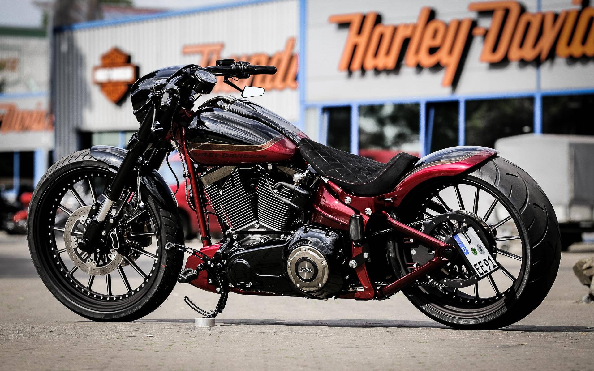 Harley 桌布 壁紙 — 一輛訂製紅黑色哈雷機車停放在經銷商外，帶有醒目的橙色招牌。