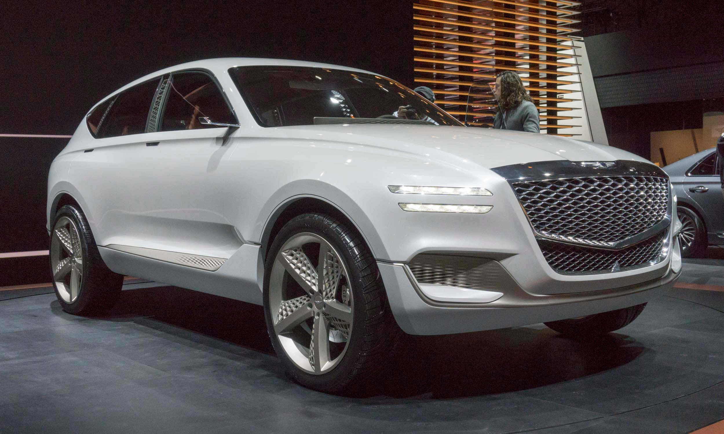 Genesis Gv80 桌布 壁紙 — 一輛設計時尚、採用未來主義風格、配備發光頭燈的白色概念SUV，在明亮的燈光下於車展中展出。