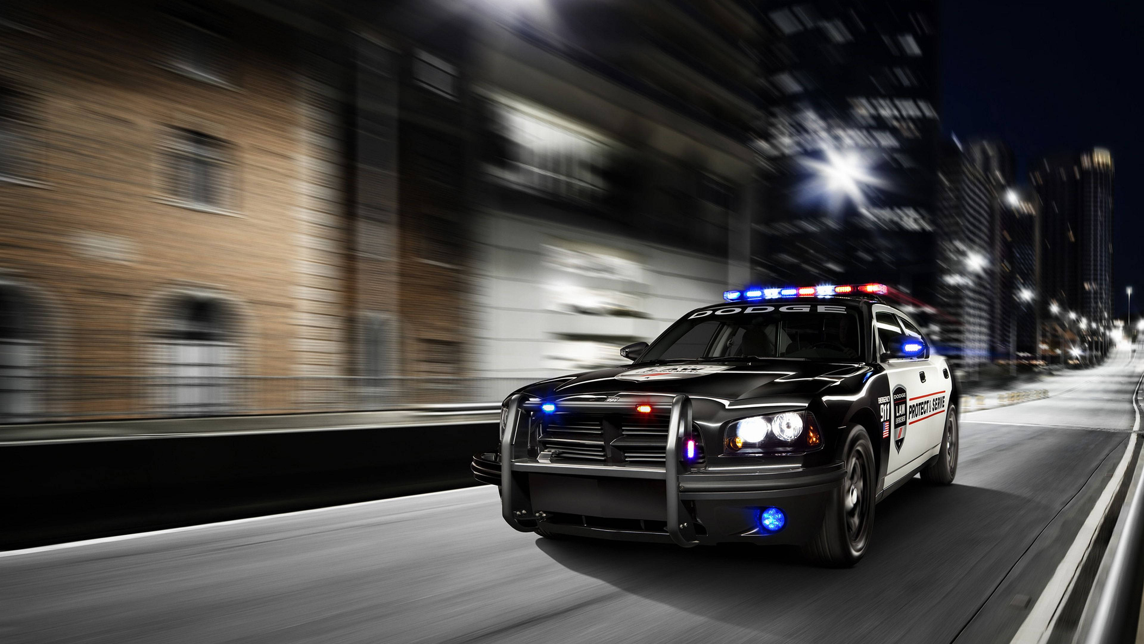 警察 桌布 壁紙 — 一輛警車在夜間穿過模糊的城市街道，伴隨著閃爍的燈光和動態模糊。