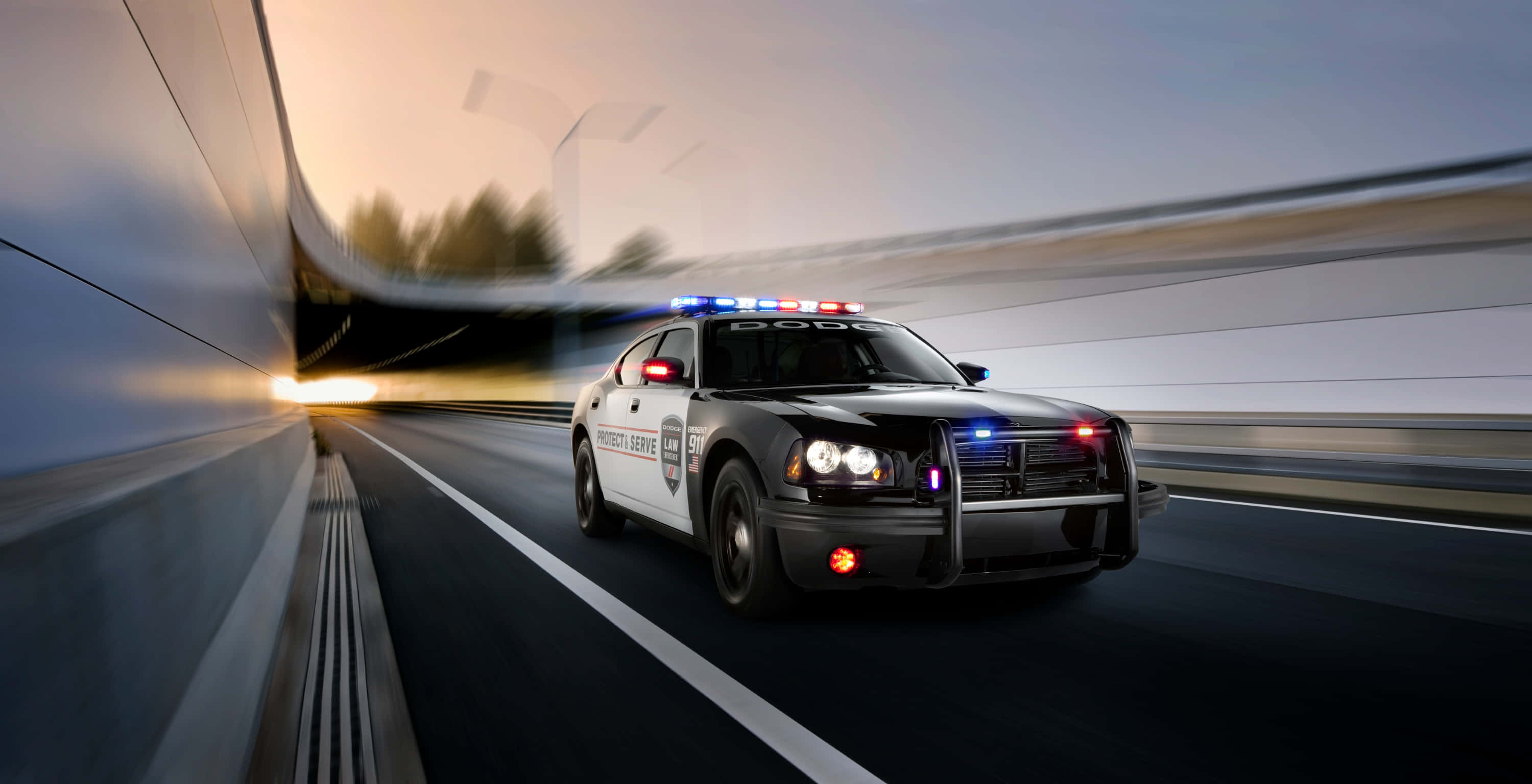 Law Enforcement 桌布 壁紙 — 一輛警車在日落時分高速駛過高速公路隧道，帶有動態模糊和閃爍燈光。