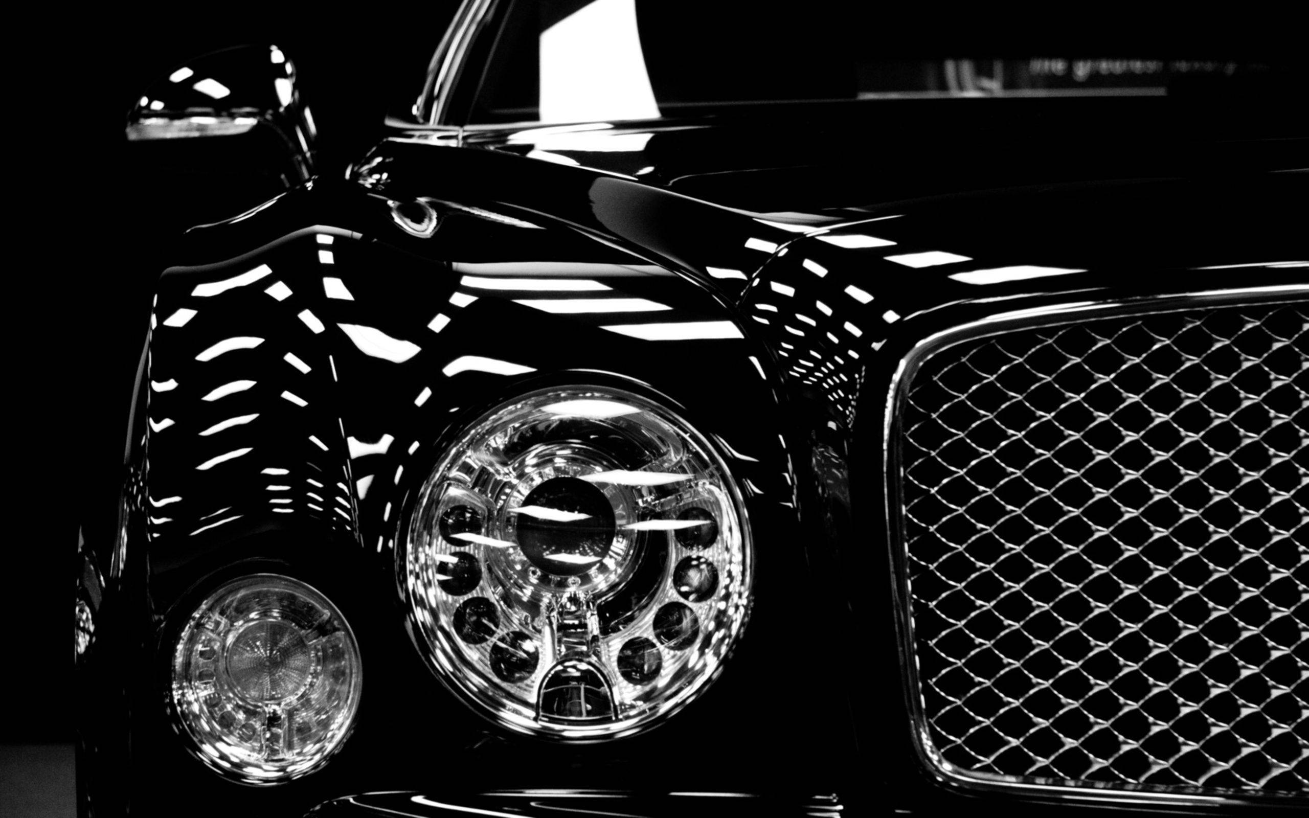 Bentley Cars 桌布 壁紙 — 一輛豪華汽車閃亮頭燈和格柵的高對比度黑白特寫，反射出銳利的幾何光圖案。