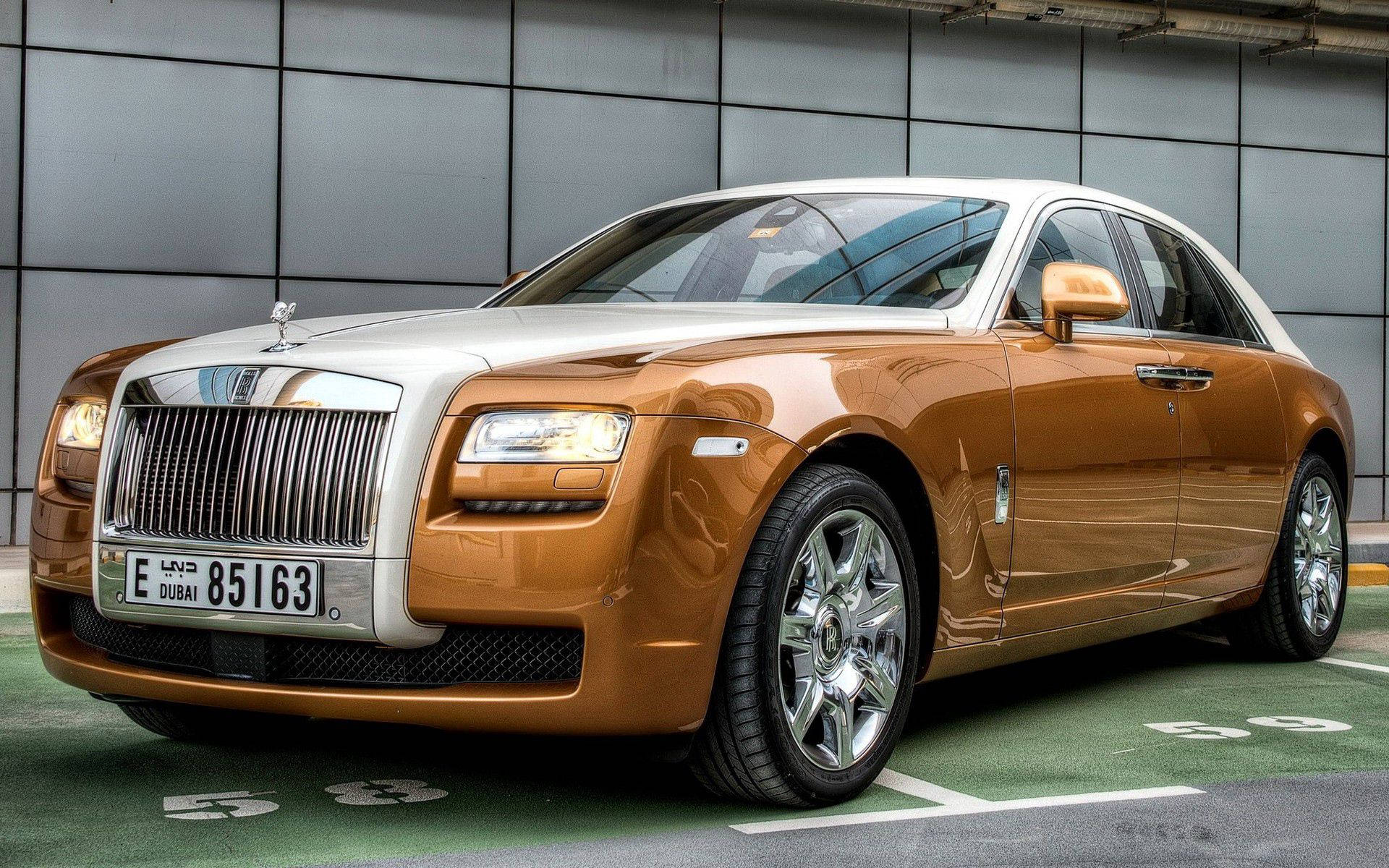Royce 桌布 壁紙 — 一輛豪華金色勞斯萊斯 Ghost 停放在現代車庫中，具有反光表面和杜拜車牌。