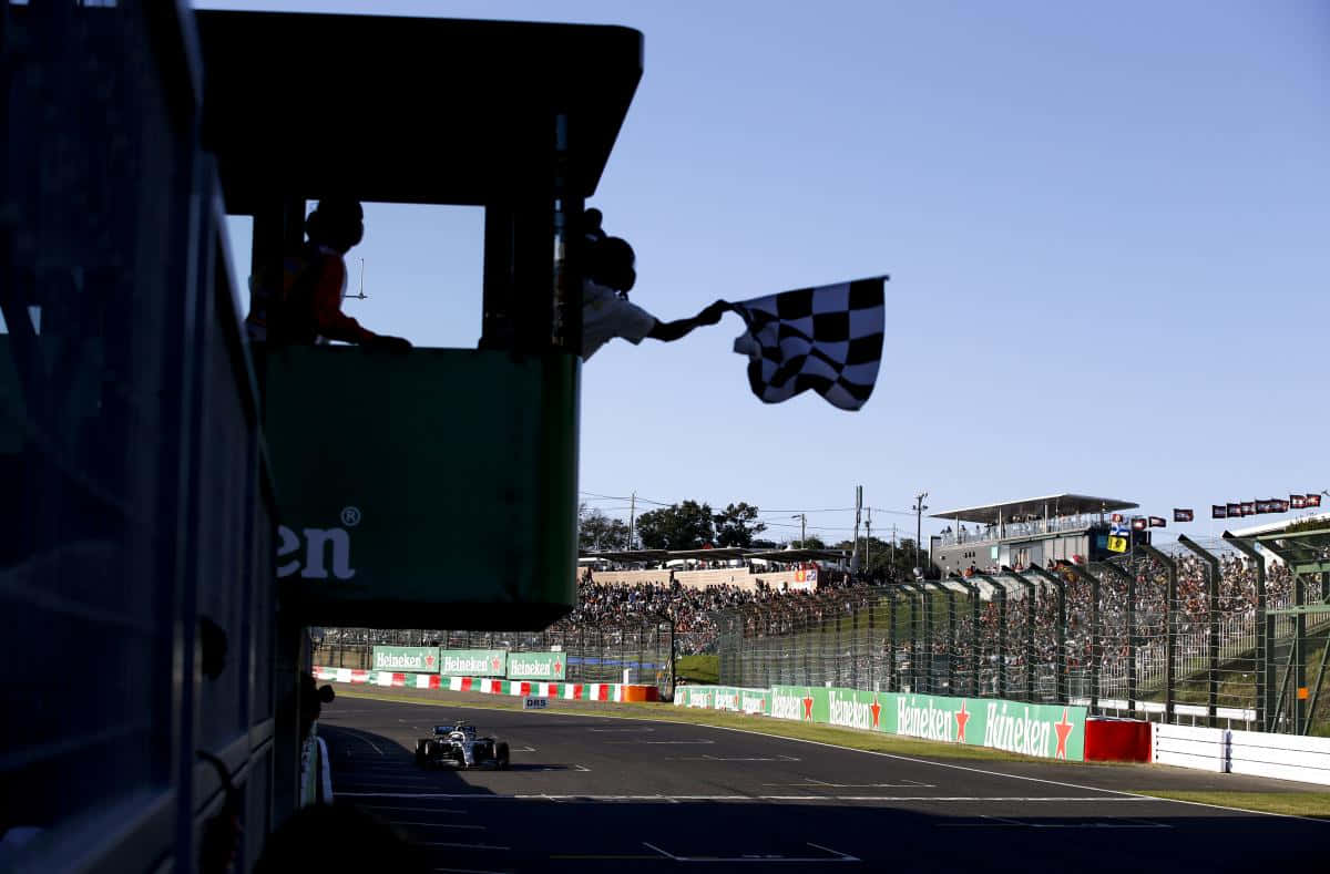 Chequered Flag 桌布 壁紙 — 一輛賽車越過終點線，塔上有人在晴朗藍天下揮動方格旗。