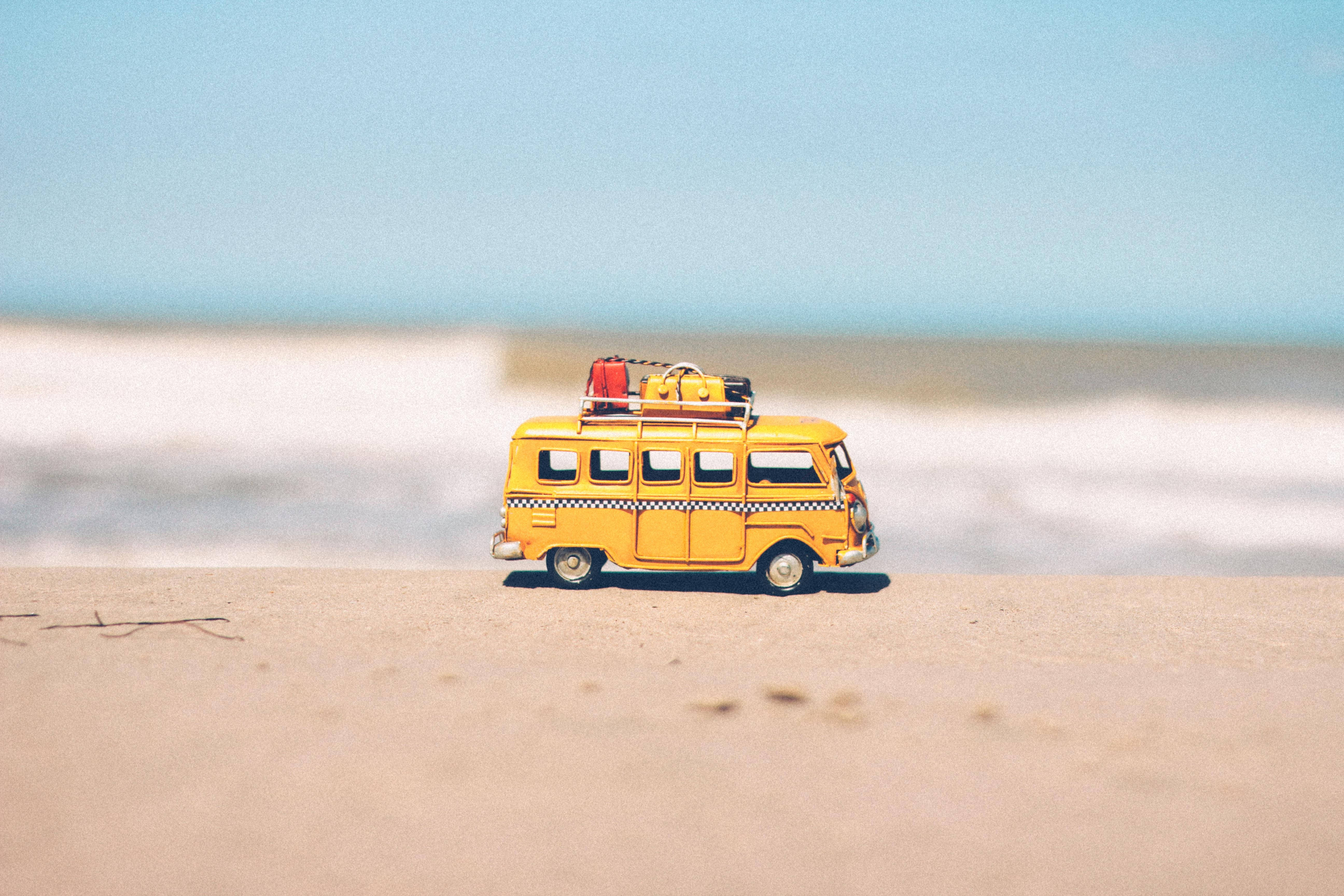 美學 桌布 壁紙 — 一輛車頂載有行李的迷你黃色復古貨車停在晴朗藍天下的沙灘上。