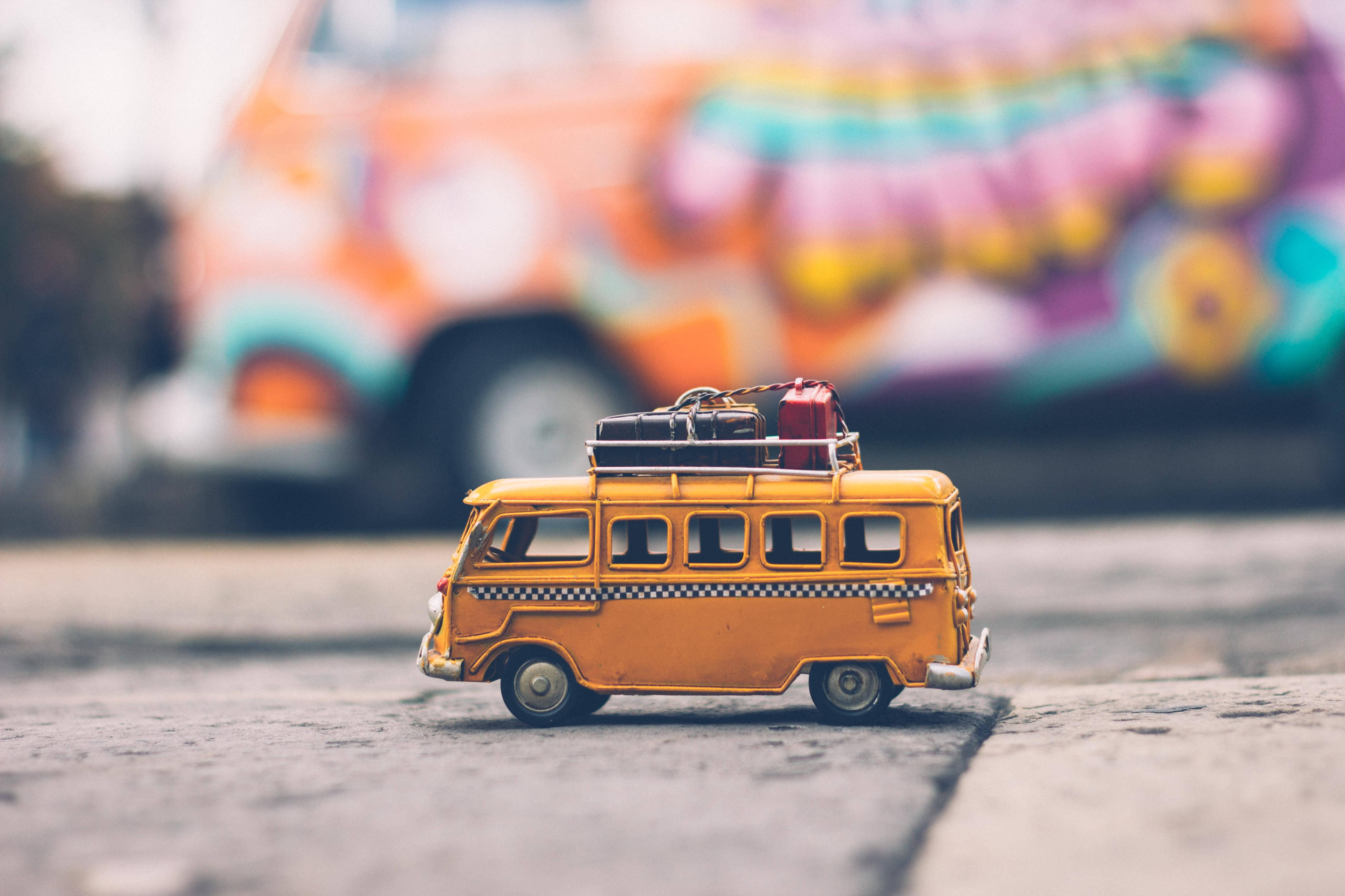 Vacation 桌布 壁紙 — 一輛迷你橙色復古貨車連同行李放在人行道上，背景中有一輛色彩繽紛的塗鴉貨車模糊可見。