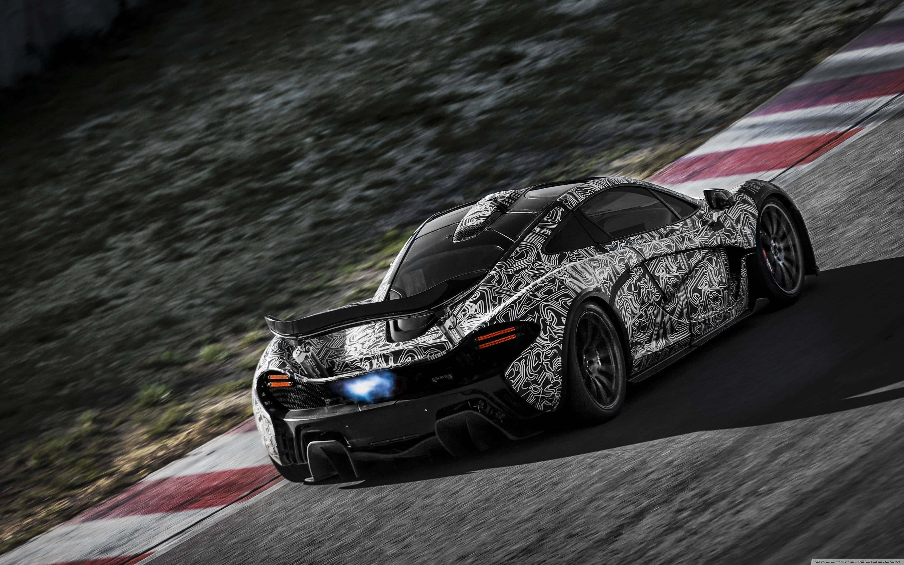 Cool Mclaren 桌布 壁紙 — 一輛迷彩塗裝的麥拉倫超級跑車在陽光普照下，沿著設有紅白路緣的賽道飛馳。