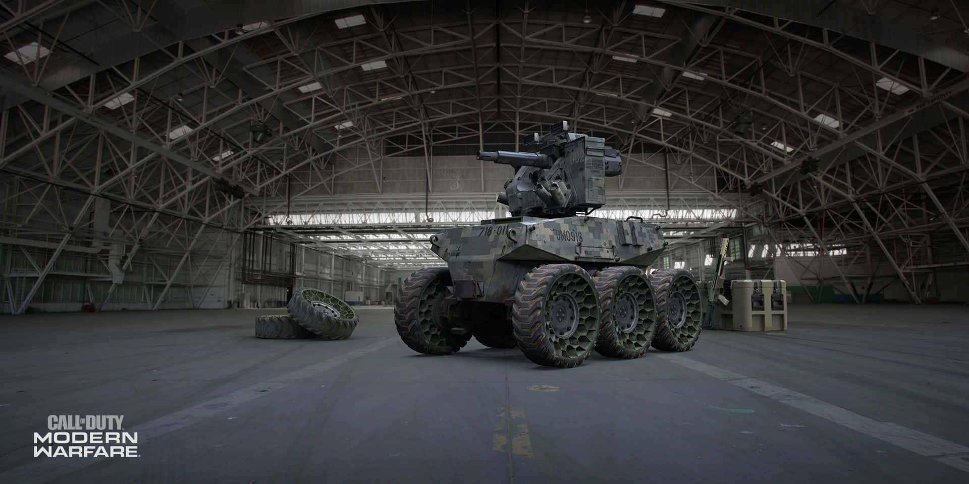 Call Of Duty Vehicles 桌布 壁紙 — 一輛迷彩裝甲車停放在一個寬敞的工業機庫內，機庫有外露的鋼桁架和昏暗的頂燈。