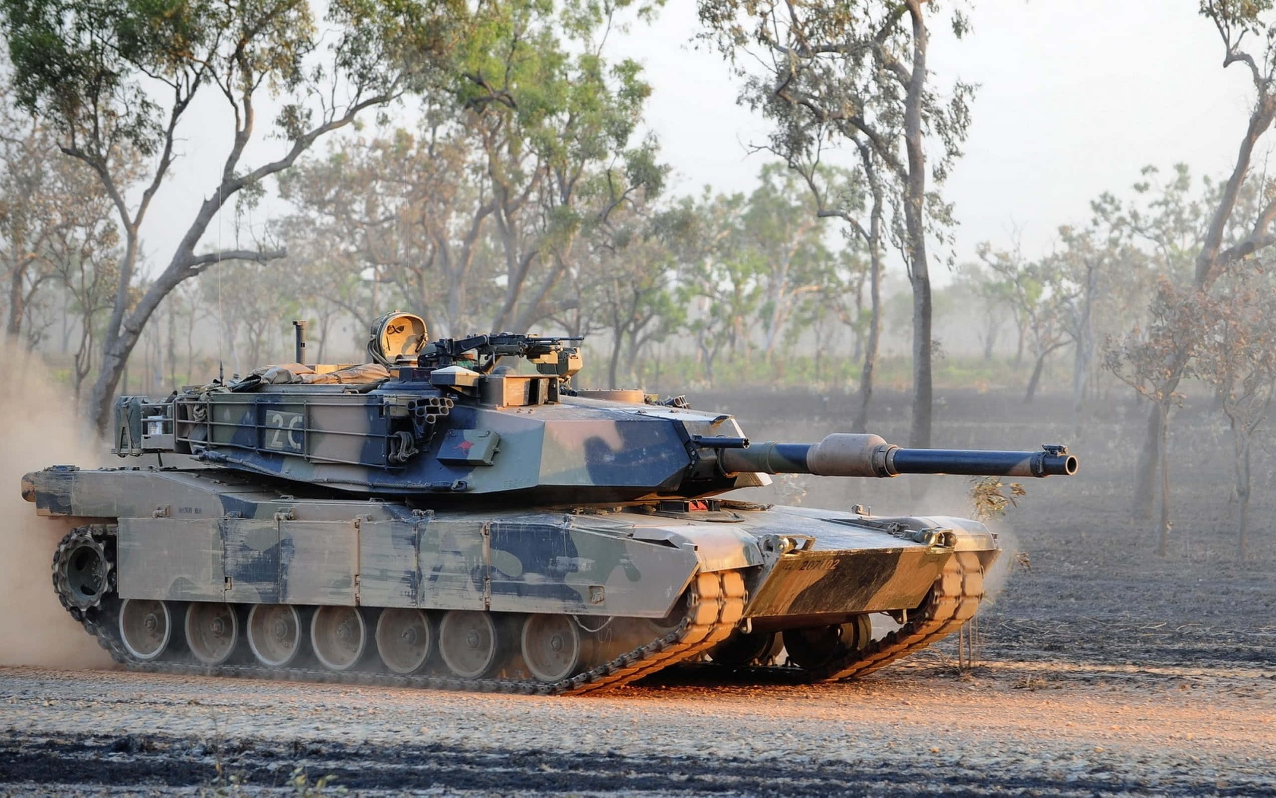 坦克 桌布 壁紙 — 一輛迷彩軍用坦克在塵土飛揚的田野中行駛，背景有稀疏的樹木。