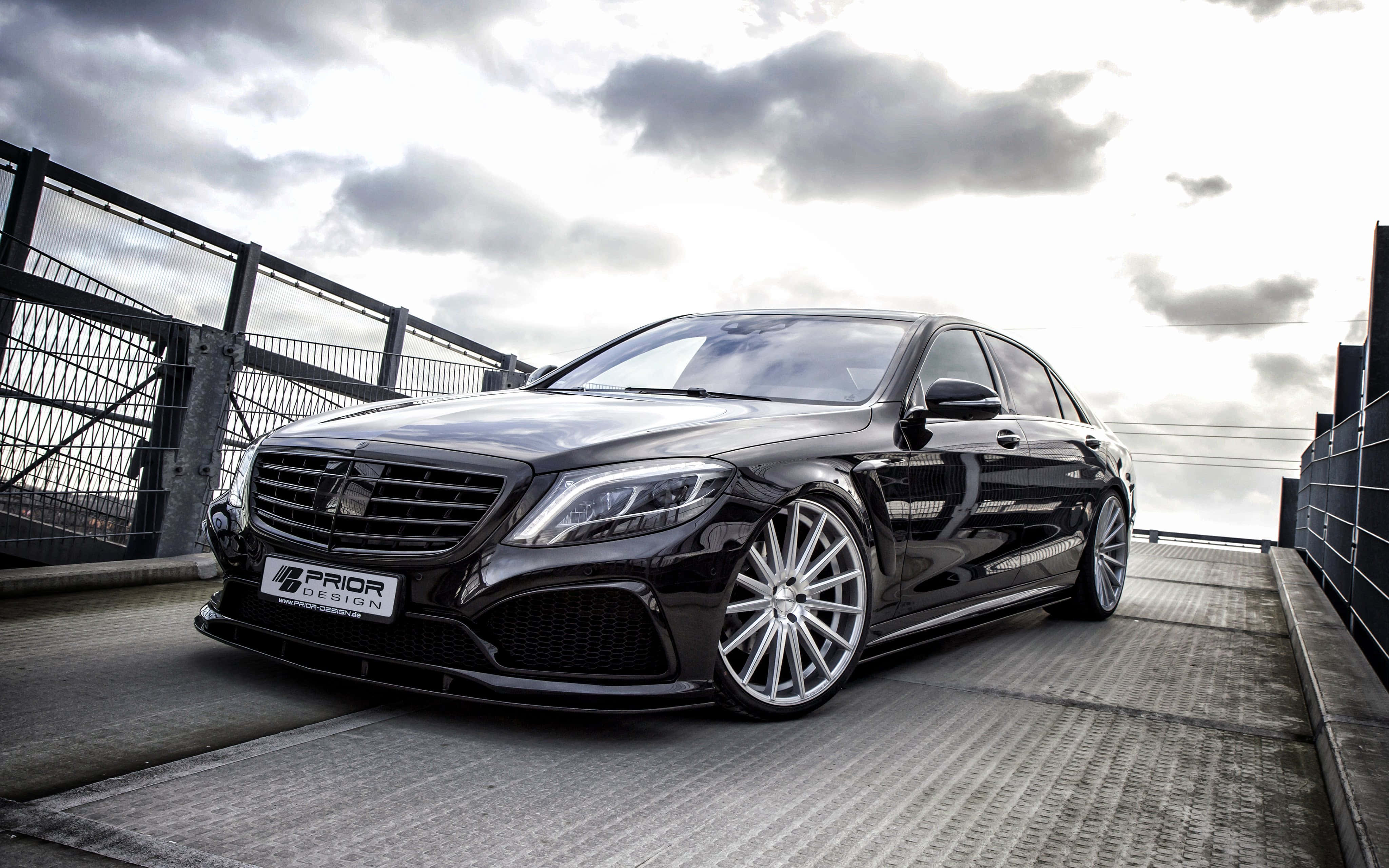 Mercedes 桌布 壁紙 — 一輛配備訂製輪圈的時尚黑色賓士轎車，在陰天下停放在金屬橋上。
