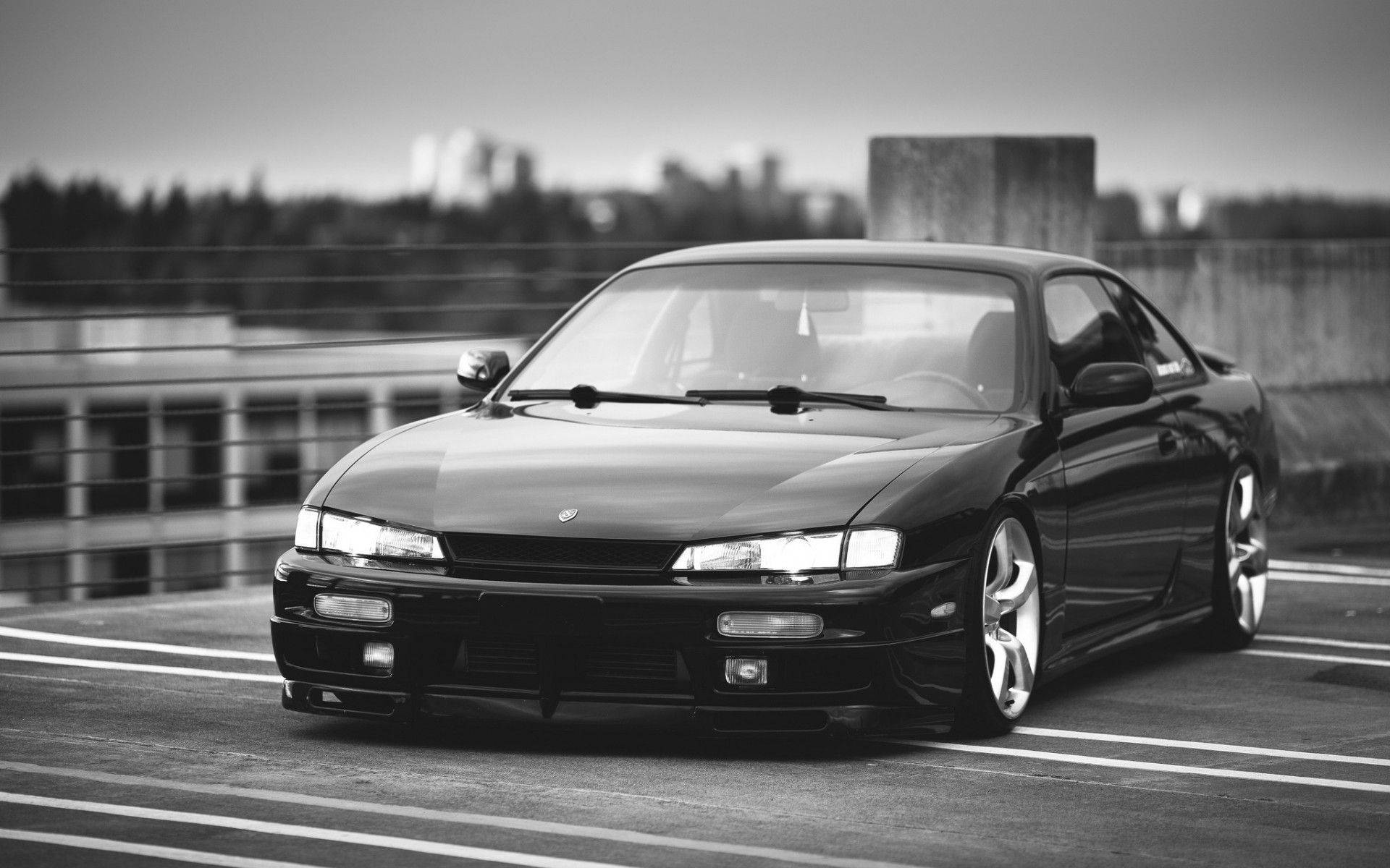 Nissan Silvia S14 桌布 壁紙 — 一輛配備訂製輪圈的時尚黑色跑車，停在高架道路上，背景是模糊的城市景觀。