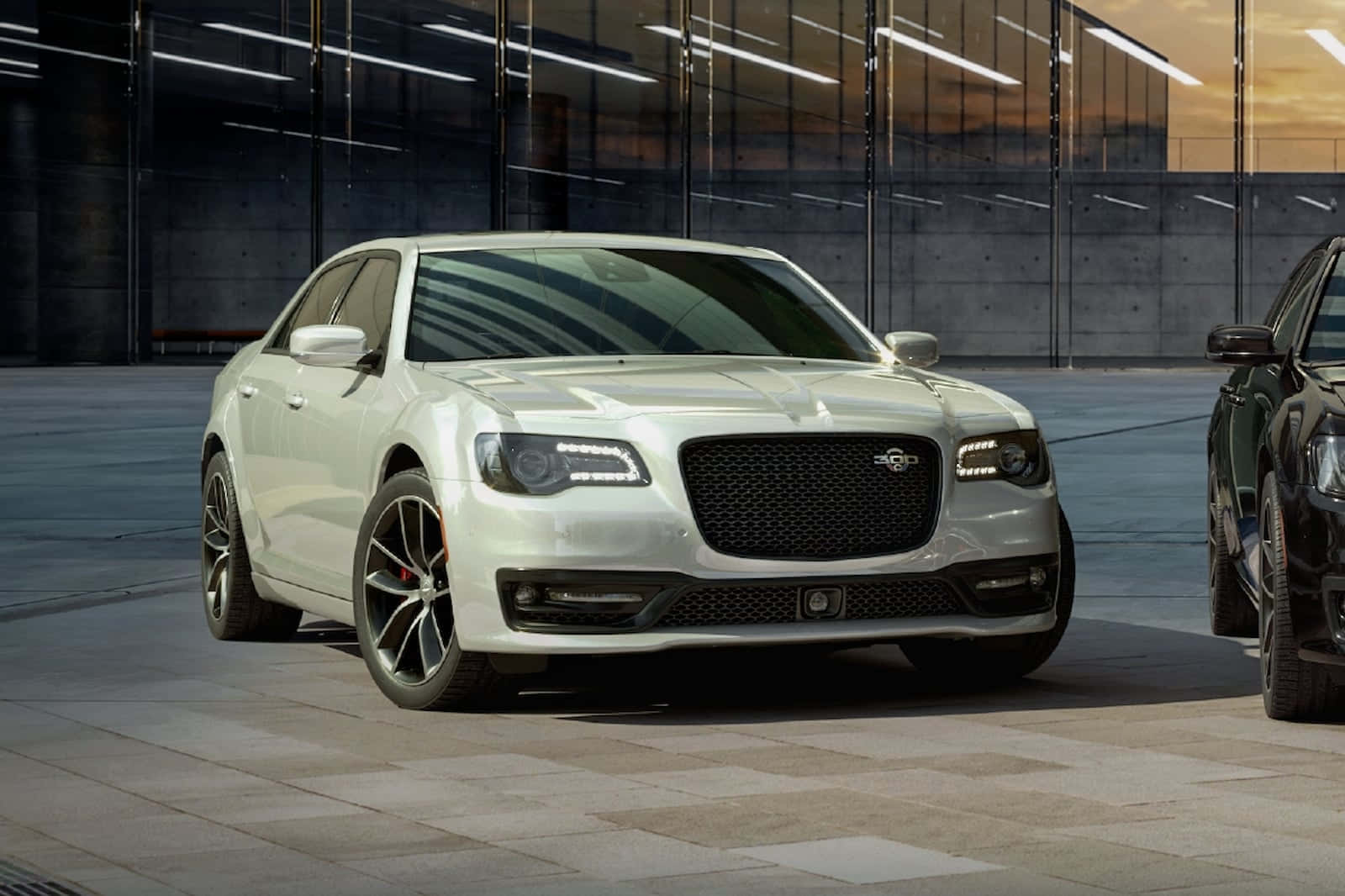 Chrysler 桌布 壁紙 — 一輛配備黑色輪圈的時尚白色豪華轎車在黃金時段停放在現代玻璃牆的城市庭院中。