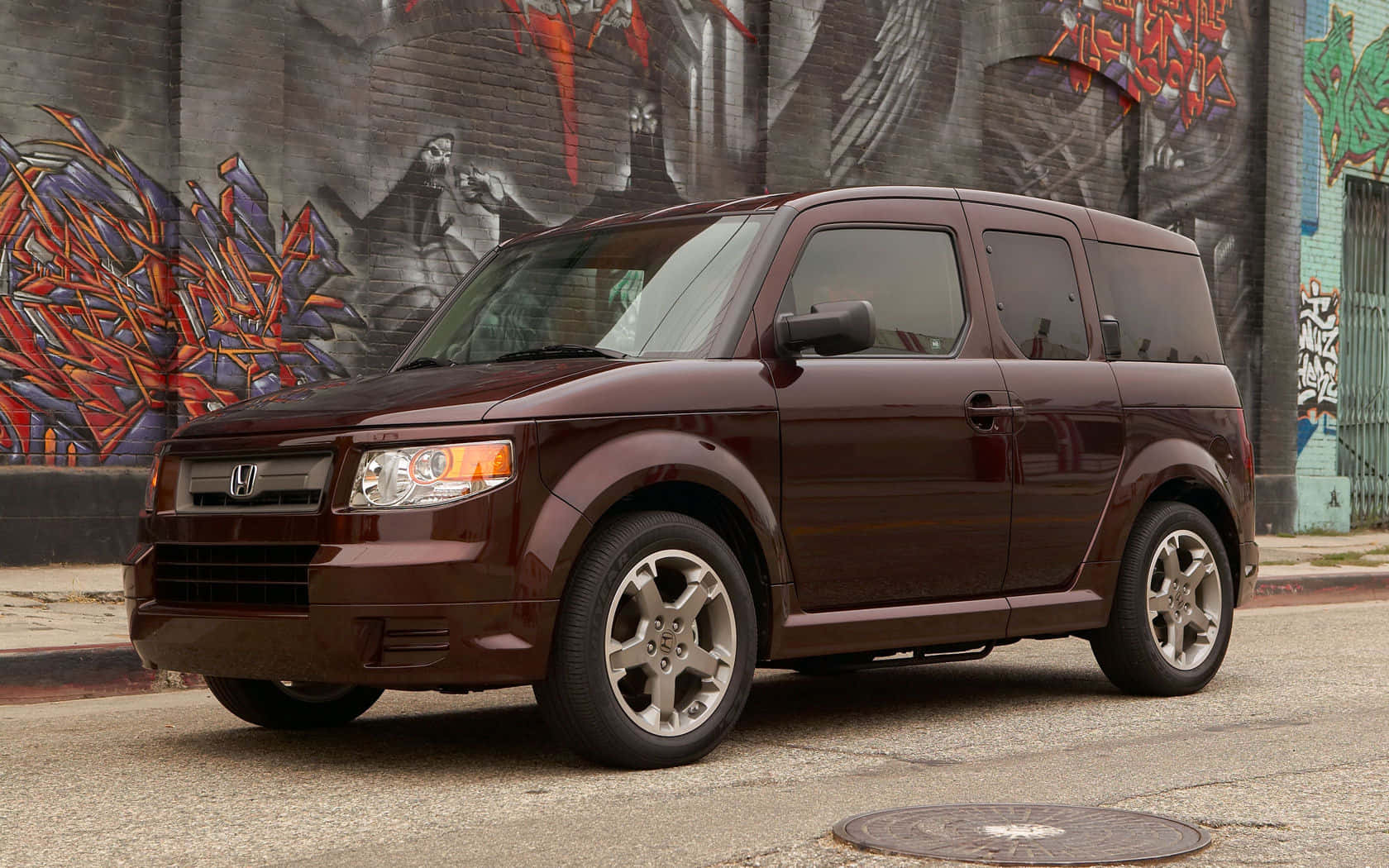 Honda Element 桌布 壁紙 — 一輛酒紅色本田 Element 停在一條佈滿砂礫的街道上，旁邊是一幅充滿活力的塗鴉磚牆。